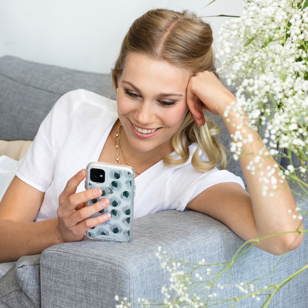 Femme tenant un téléphone, souriante, avec des fleurs en arrière-plan.