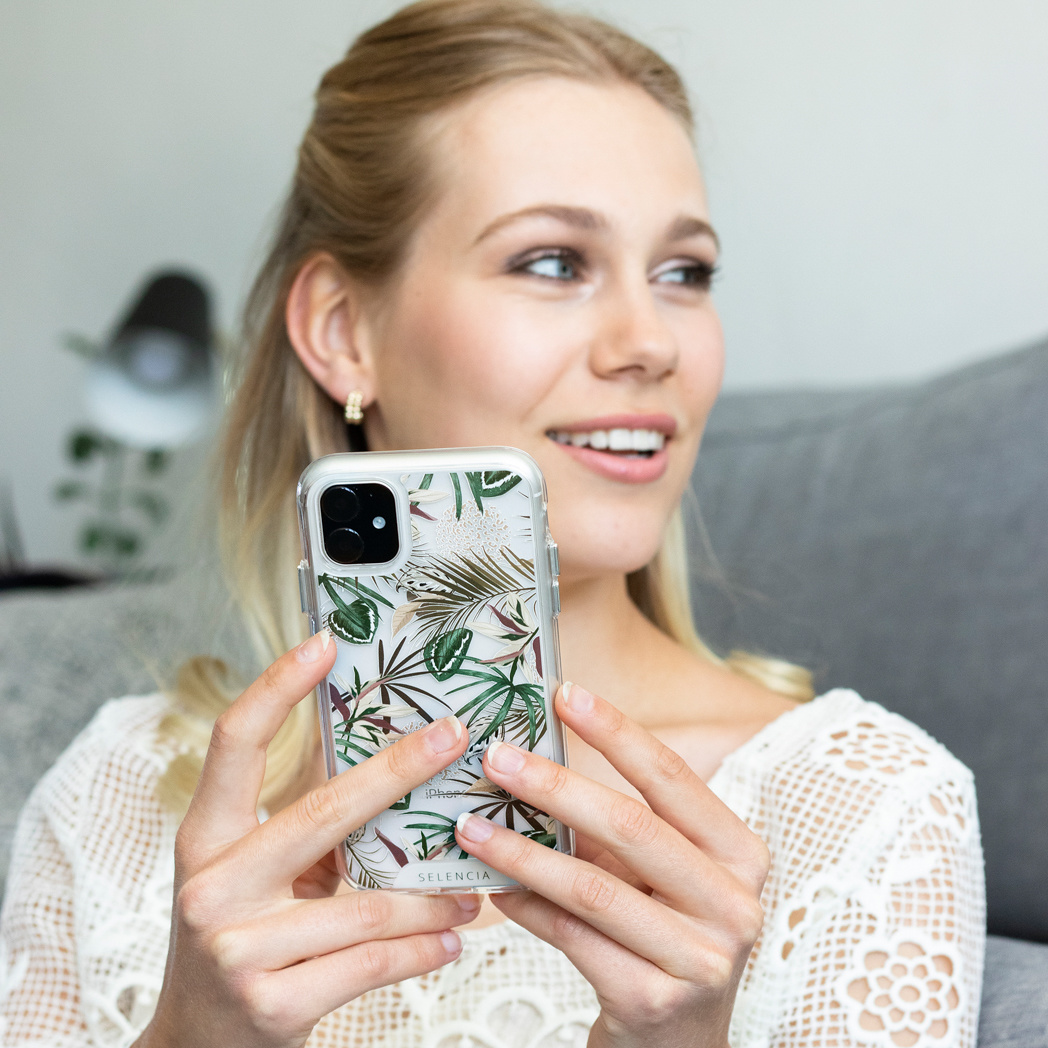 Une femme tenant une coque de téléphone transparente avec un motif botanique, souriant sur le côté.
