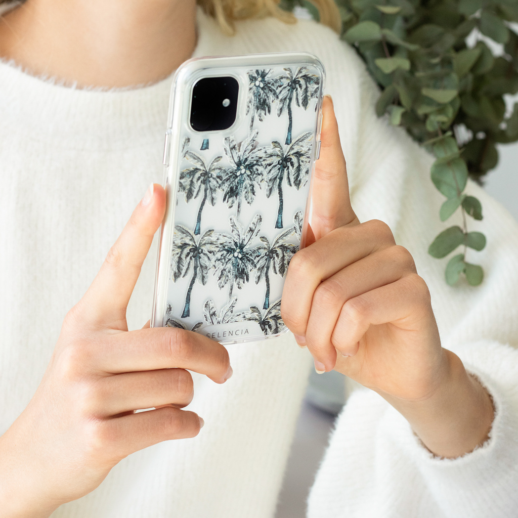 Personne tenant un téléphone avec une coque de palmiers ; autres poupées en arrière-plan.