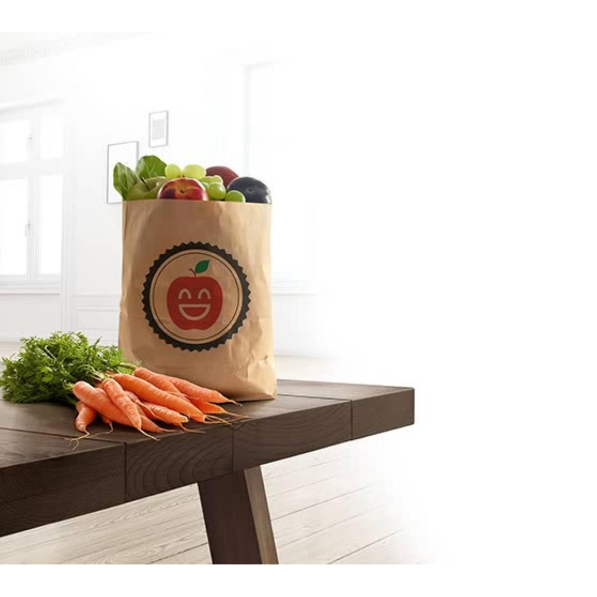Brązowa papierowa torba wypełniona artykułami spożywczymi na drewnianym stole, obok marchewki.