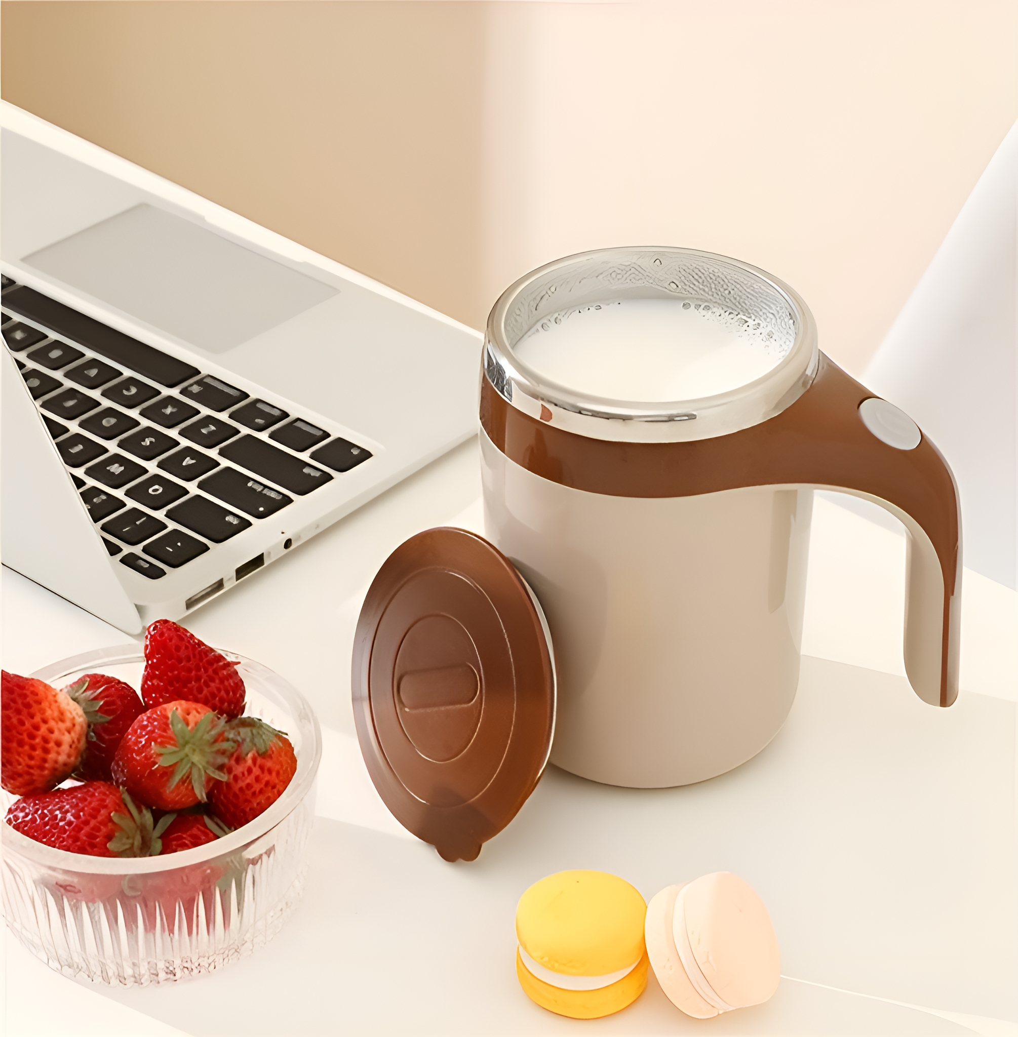 Becher mit Henkel, Deckel und Erdbeeren neben Laptop und Macarons. Auf weißer Oberfläche.