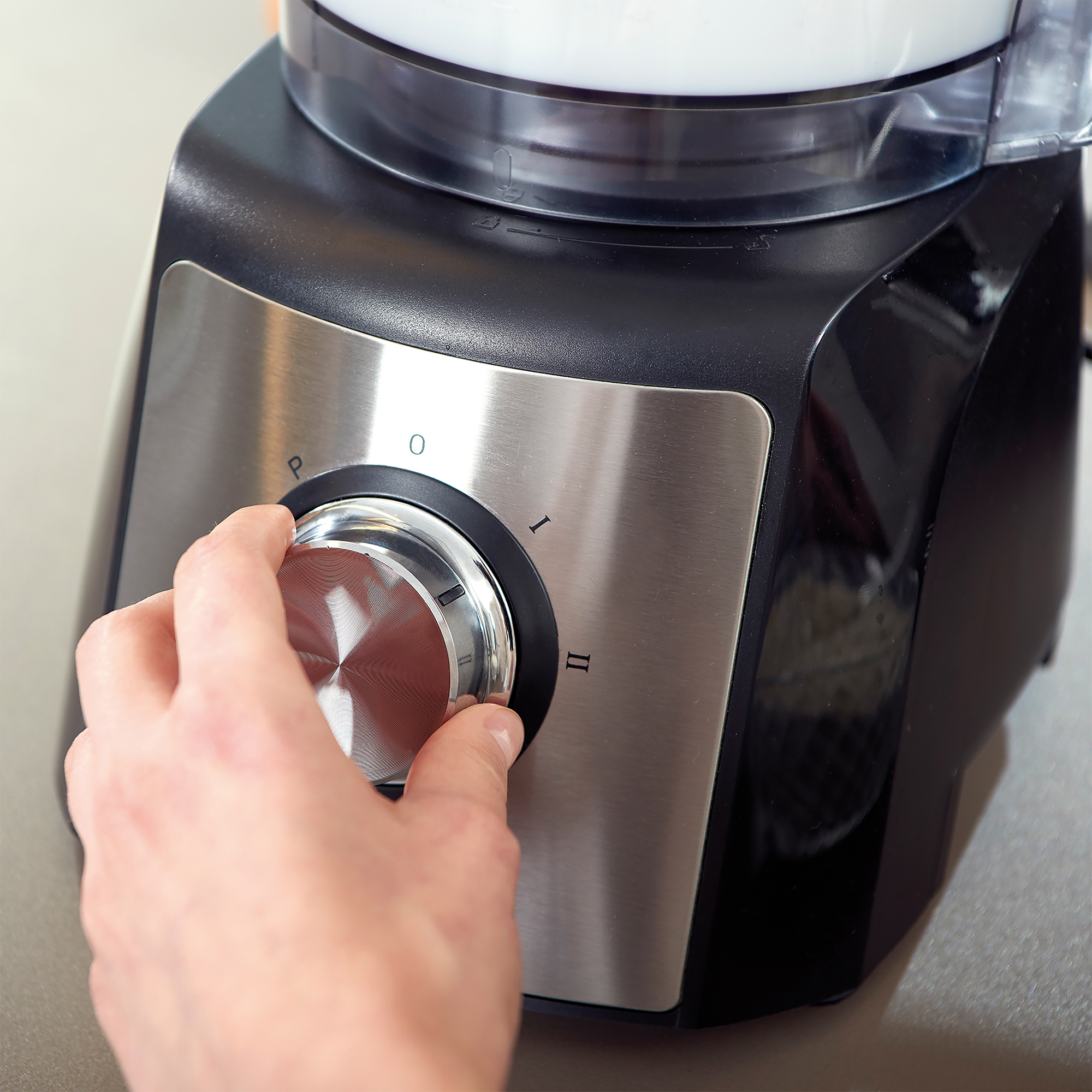 Ręka kręci srebrnym pokrętłem na robocie kuchennym. Pokrętło ma numery.