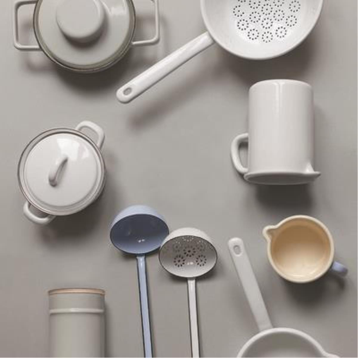 Verschiedene weiße Küchenutensilien auf grauer Oberfläche, darunter Töpfe, Schöpflöffel und eine Tasse.