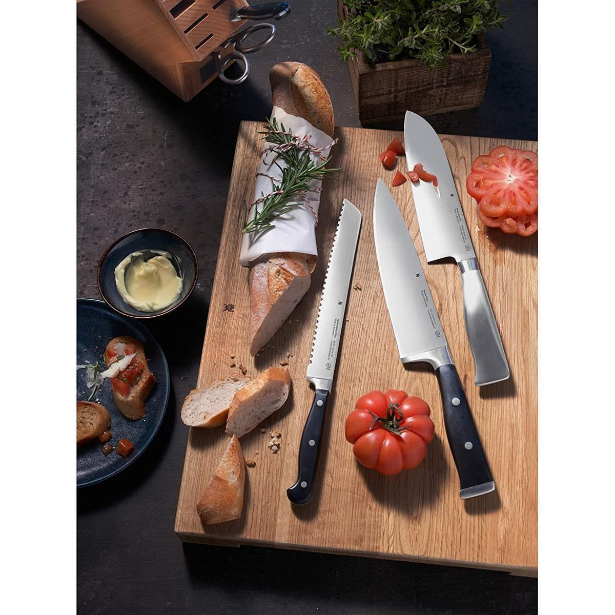 Holzschneidebrett mit Brot, Tomaten, Messern und Butter. Draufsicht.