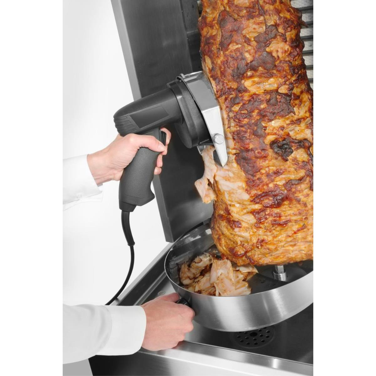 Una persona taglia carne da uno spiedo rotante con un coltello elettrico.
