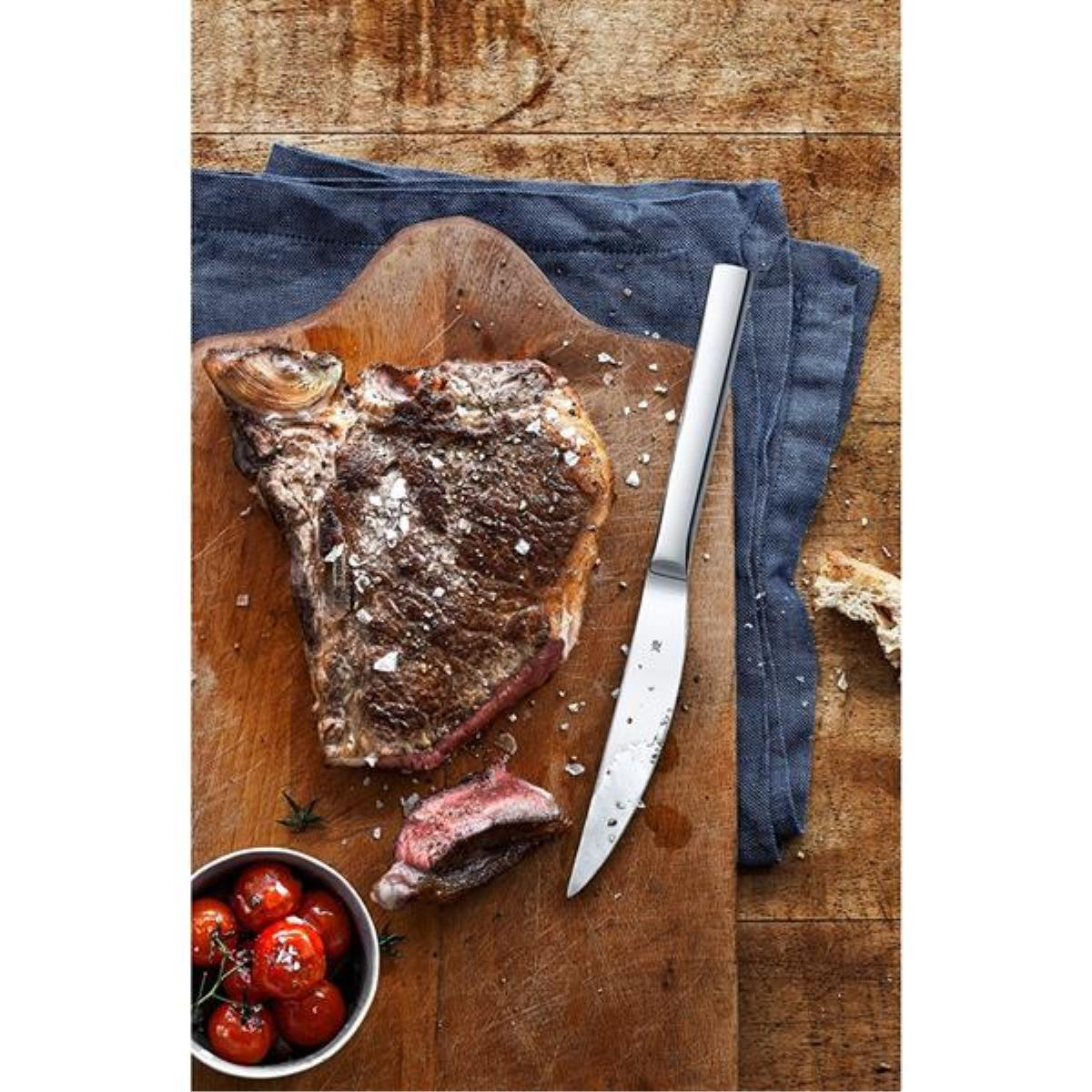 Steak, Tomaten und ein Messer auf einem hölzernen Schneidebrett mit einem blauen Tuch.