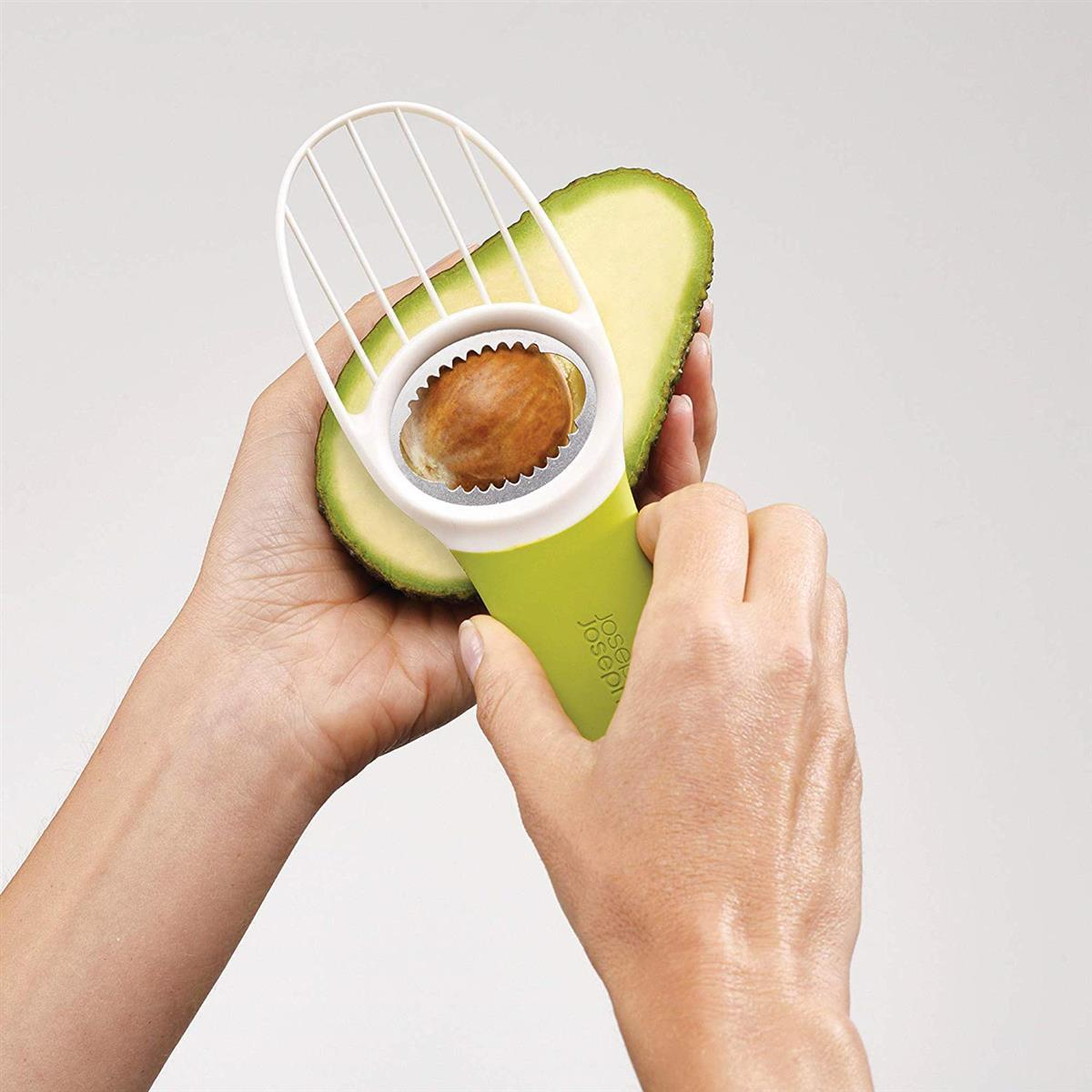 Manos usando un cortador de aguacate verde y blanco para cortar un aguacate.