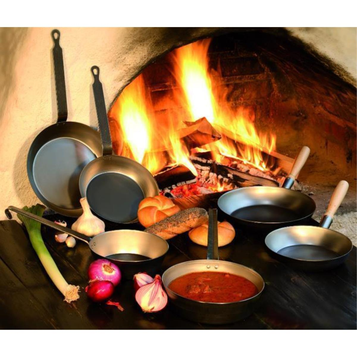 Pfannen verschiedener Größen, Brot und Gemüse vor einem Kamin mit Feuer.