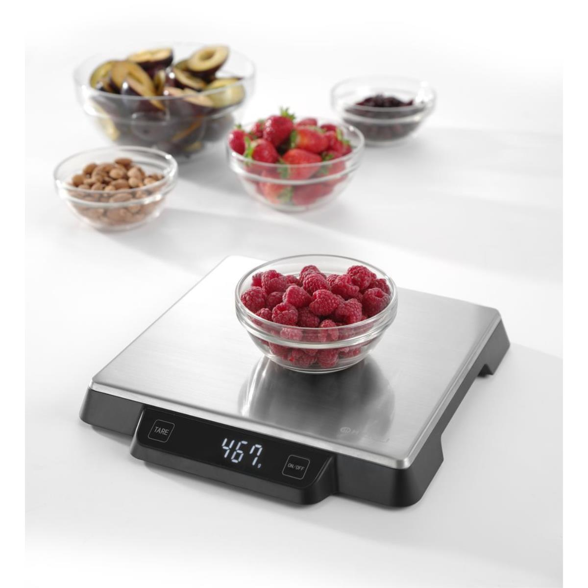 Waage mit Himbeeren und andere Schalen mit Früchten auf weißer Oberfläche.