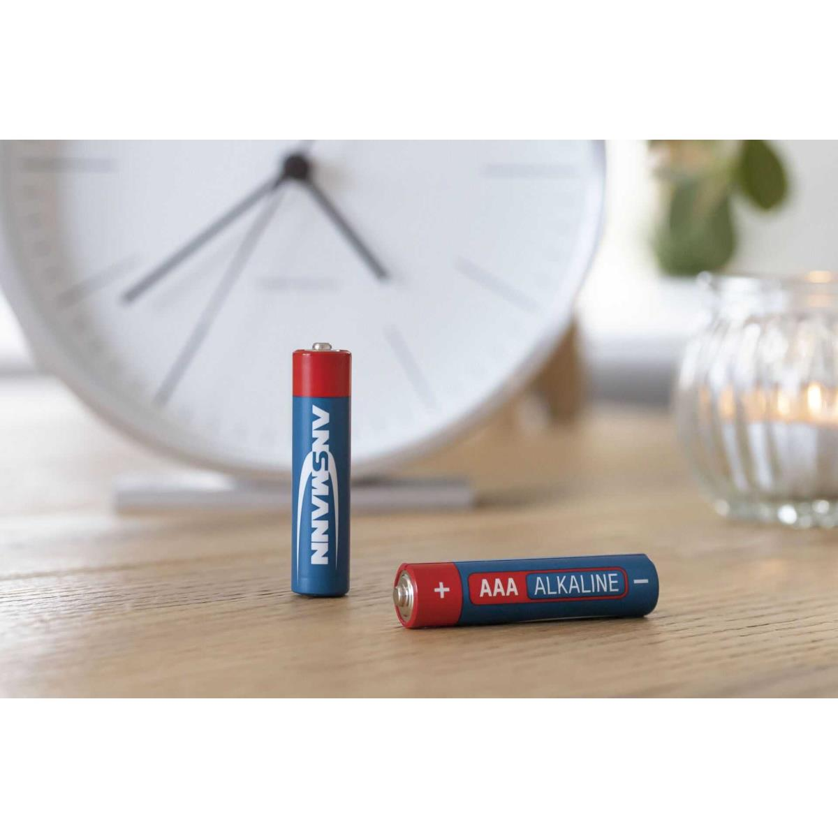 Dwie baterie alkaliczne AAA, jedna stojąca, druga płaska, na drewnianej powierzchni. Zegarek jest rozmyty w tle.