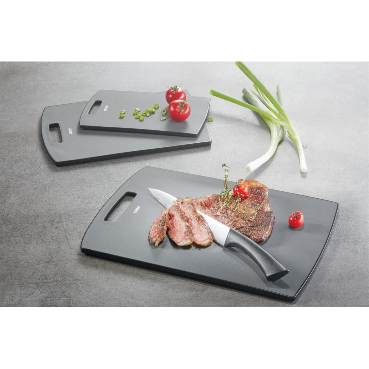 Schneidebretter mit Steak, Messer, Tomaten und Frühlingszwiebeln. Zwei Bretter, eines mit Essen.