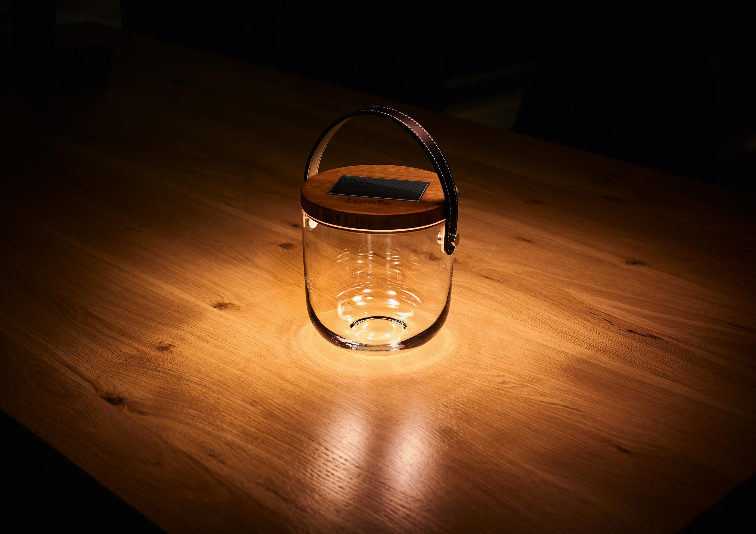 Eine Glaslaterne mit Holzdeckel und Ledergriff, die auf einem Holztisch steht.