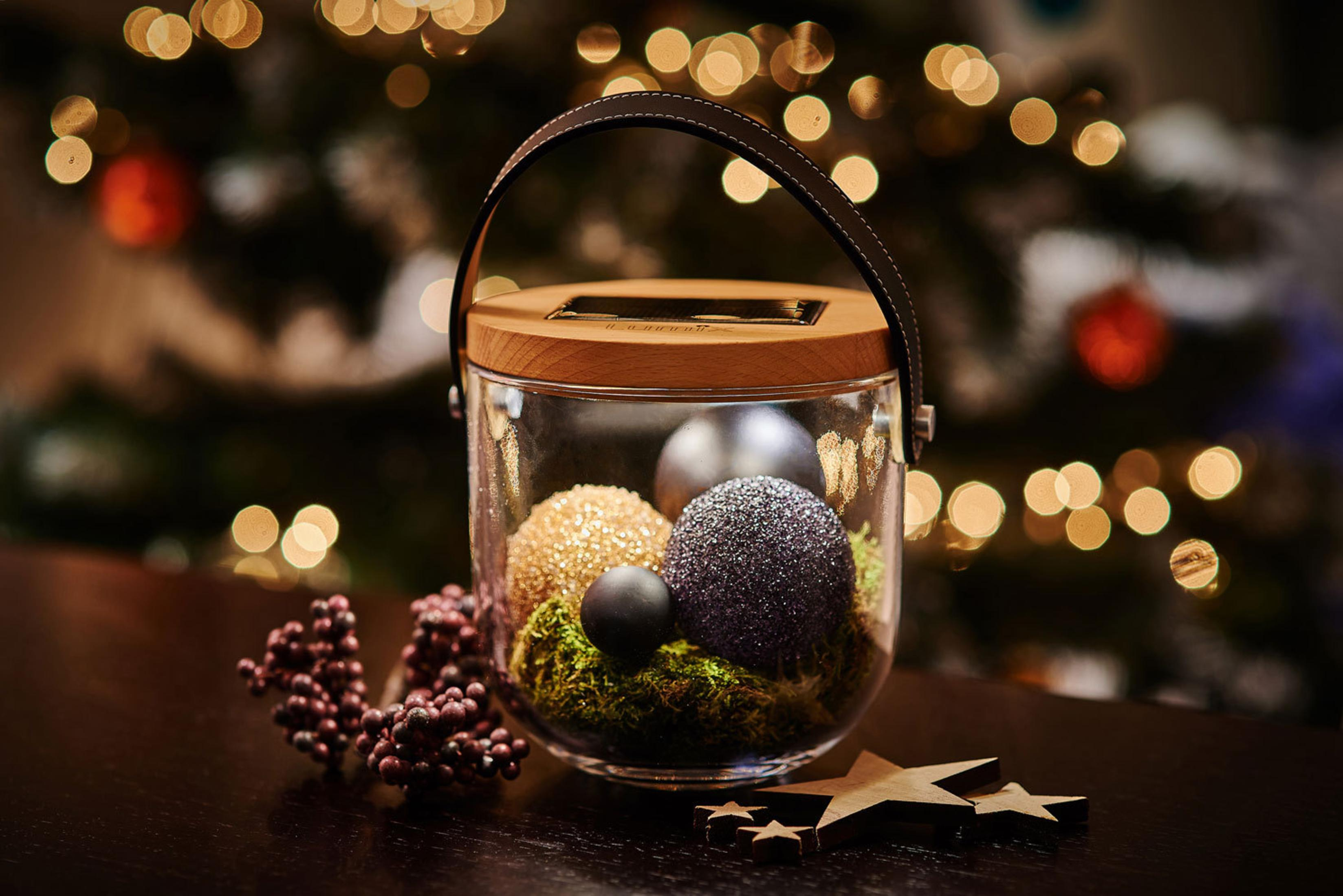 Ein Glasbehälter mit dekorativen Weihnachtskugeln und einem Holzstern auf einem Tisch.
