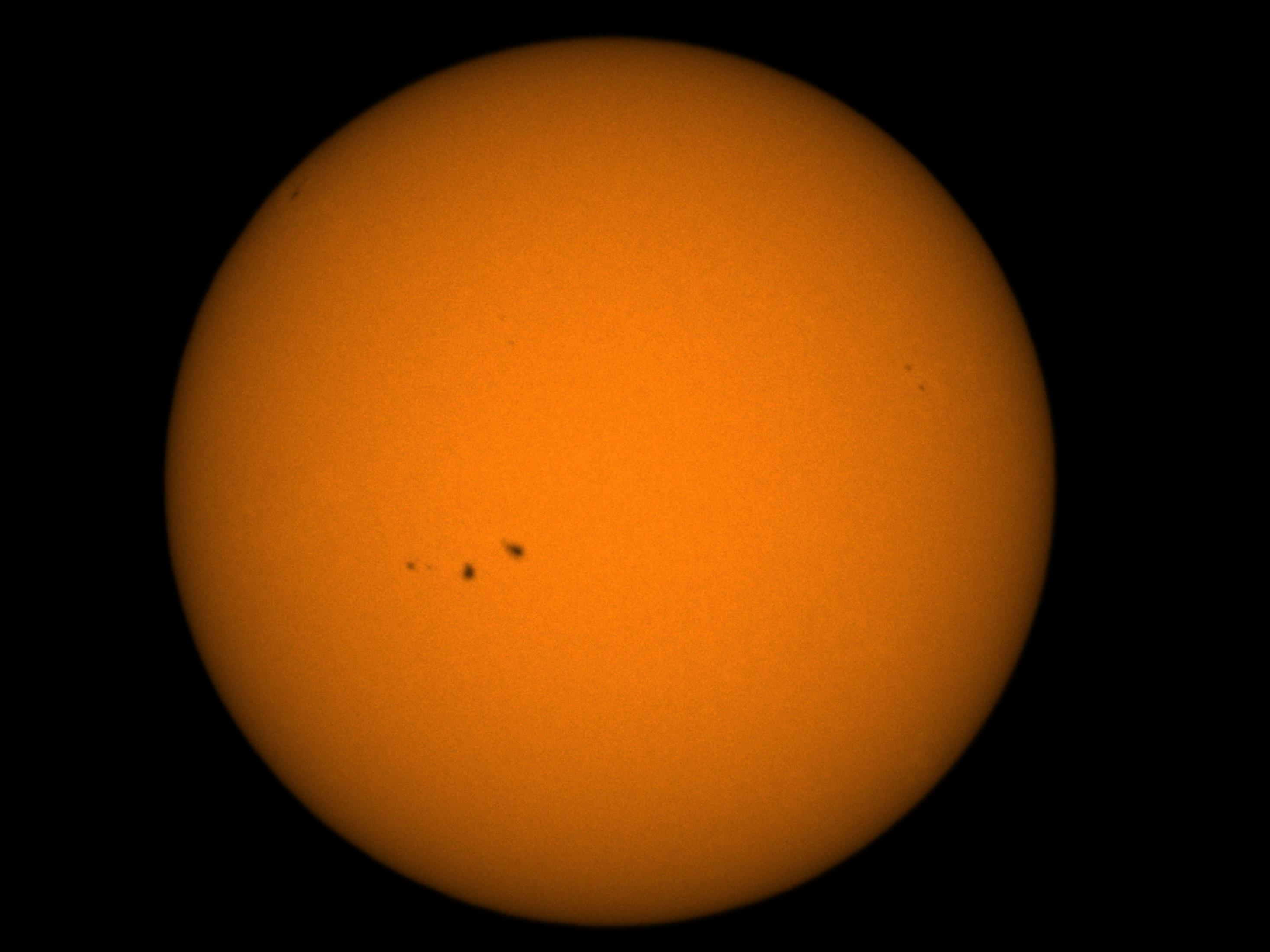 Orangefarbene Sonne mit Sonnenflecken, vor einem vollständig schwarzen Hintergrund.