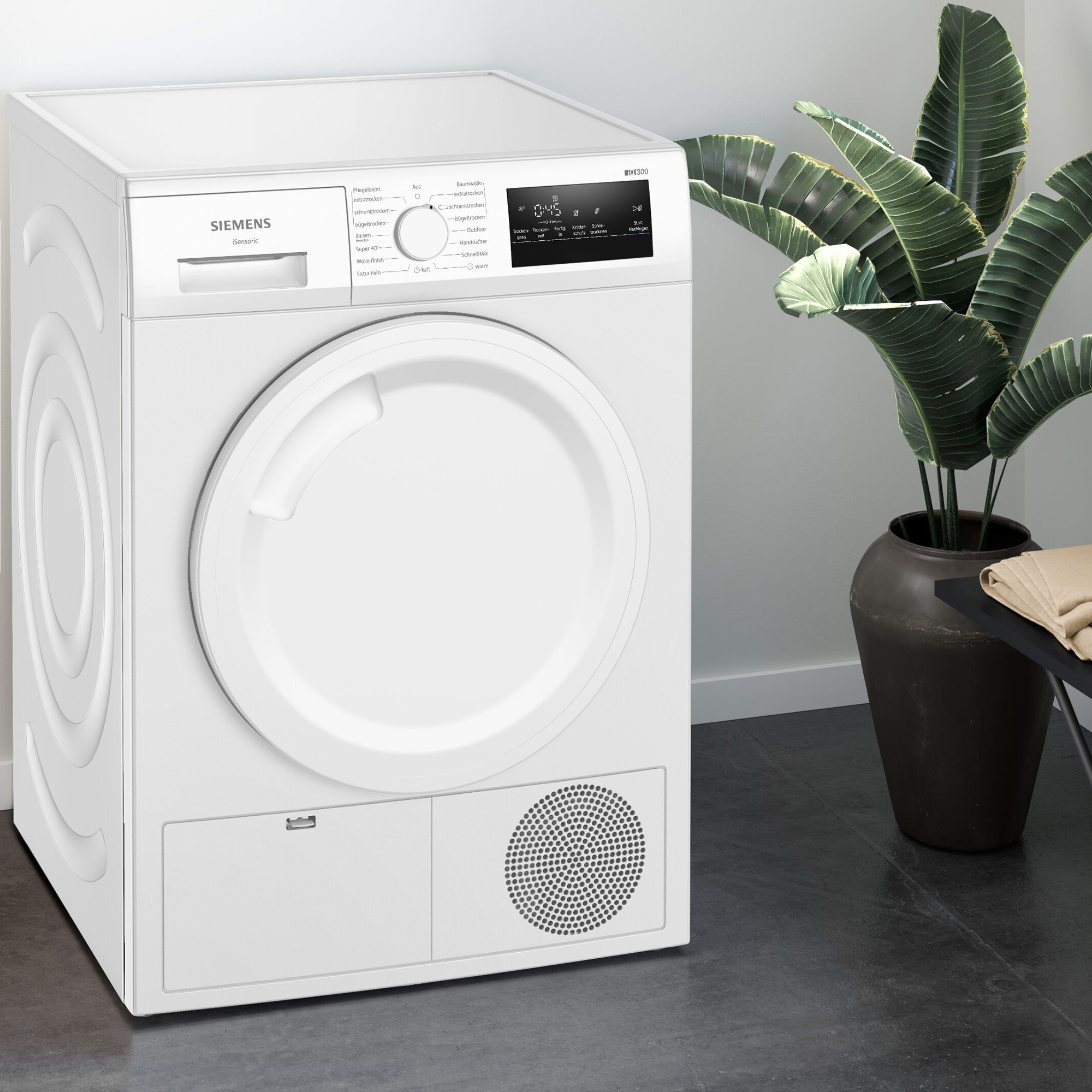 Biała suszarka Siemens z panelem sterowania, obok dużej rośliny.
