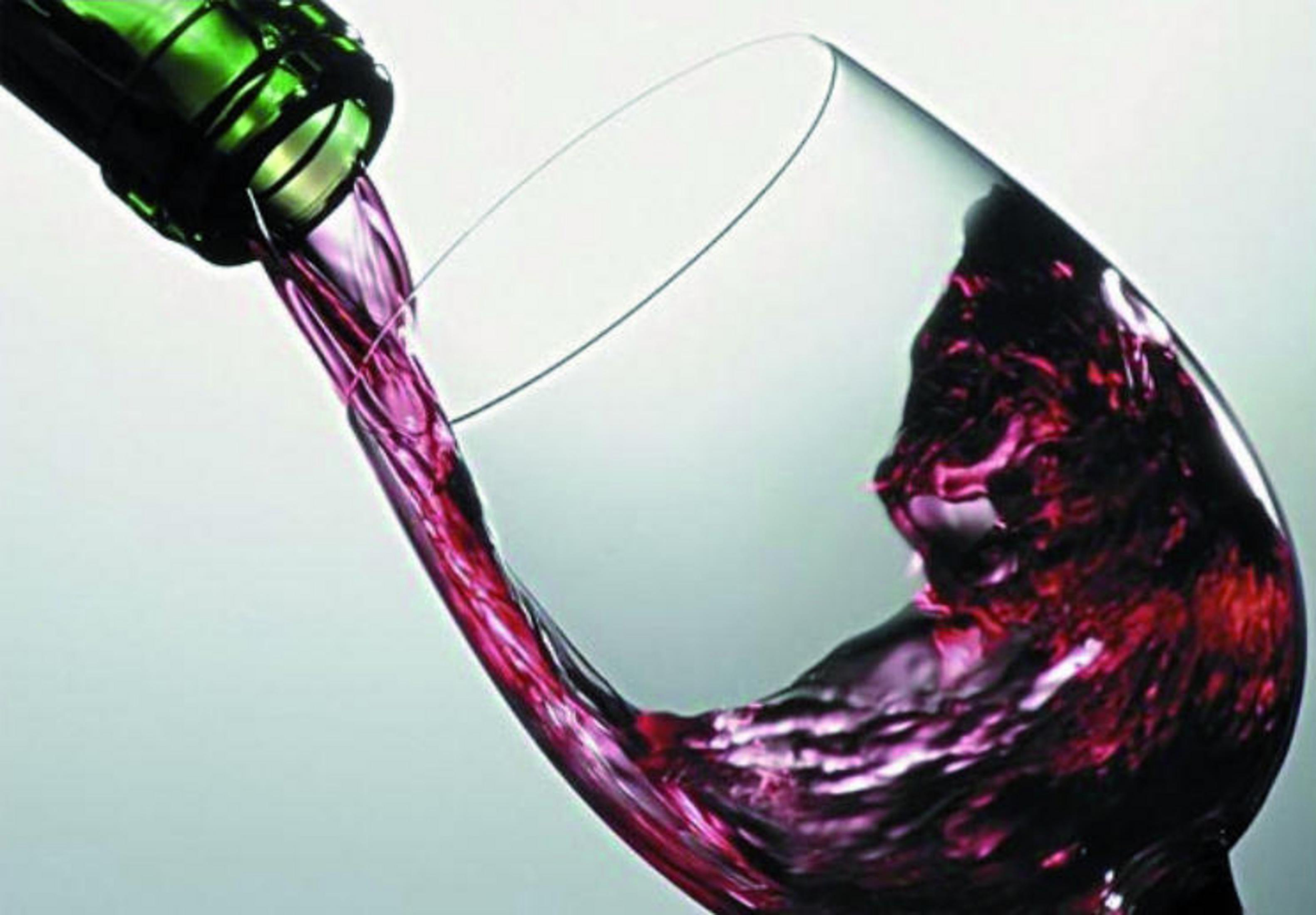 Rotwein wird in ein Weinglas gegossen. Das Glas ist geneigt. Weiß bis grauer Hintergrund.