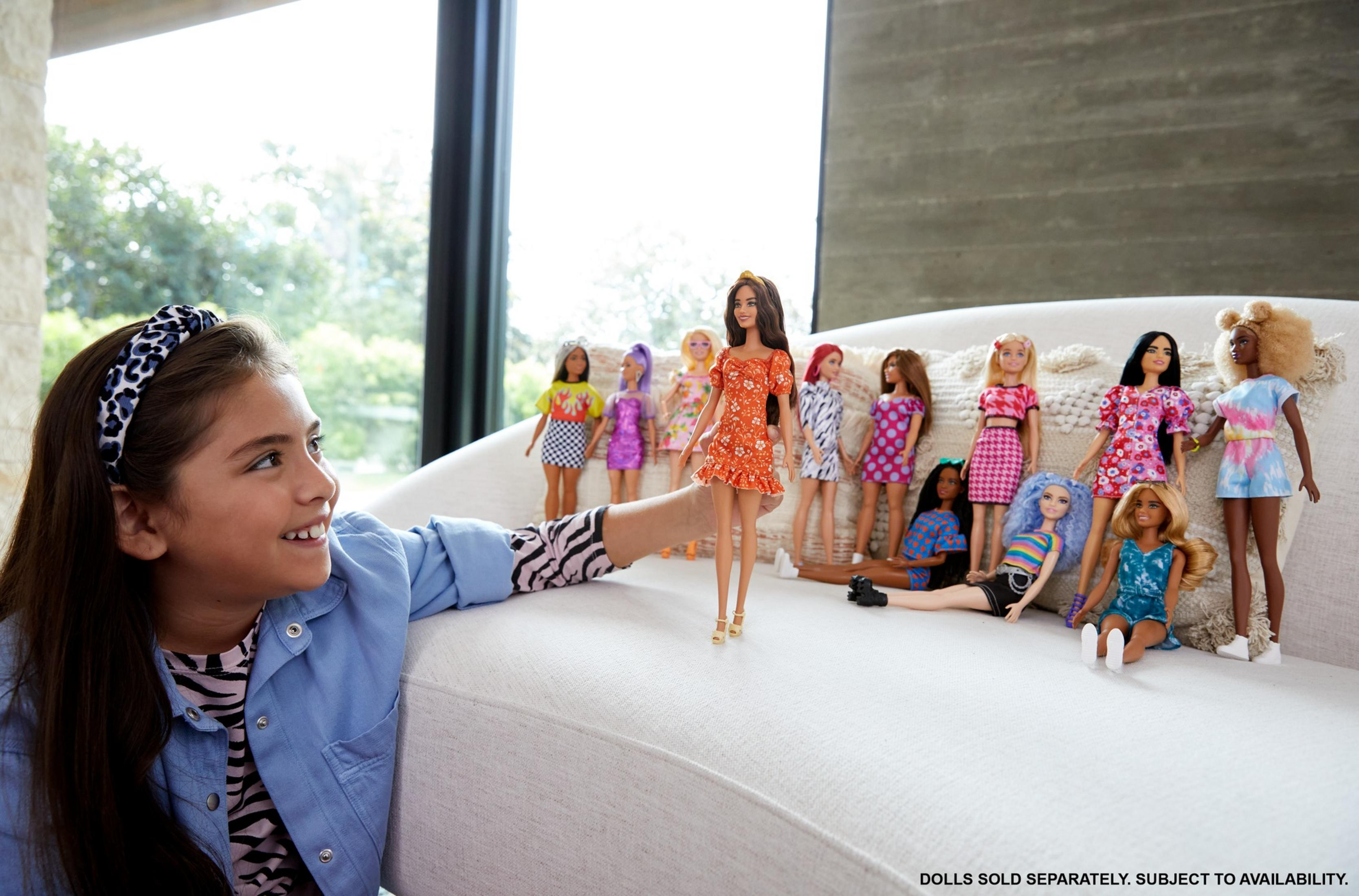 Ein Mädchen und viele Barbie-Puppen auf einem Sofa, mit verschwommenem Hintergrund.