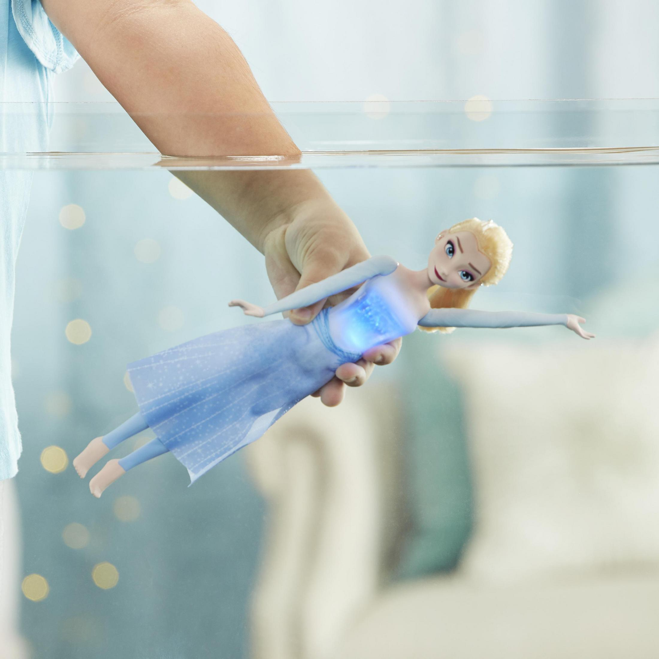 Eine Puppe schwimmt im Wasser, gehalten von einer Hand. Es ist eine Elsa-Puppe, mit blauem Kleid.