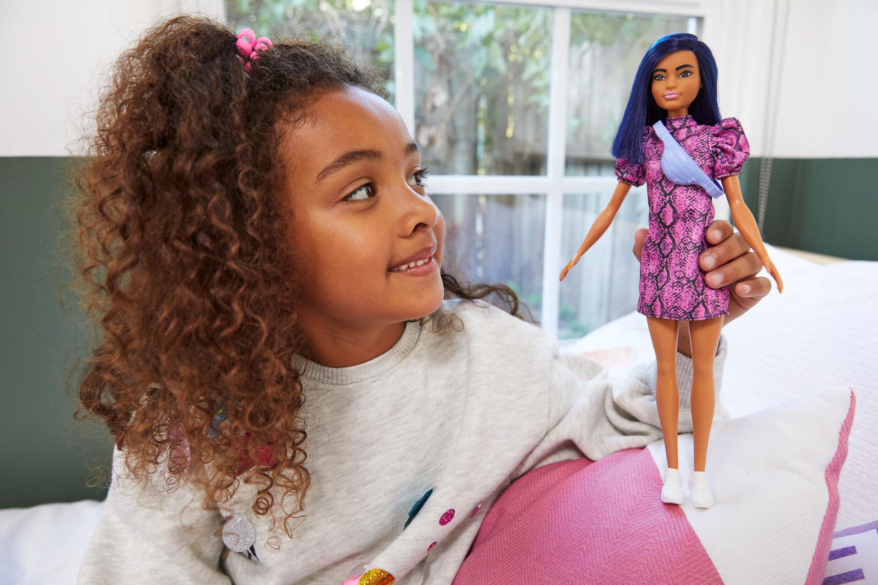 Ein Mädchen, das eine Barbie-Puppe mit rosa Kleid und eine Puppe mit blauem Kleid betrachtet.