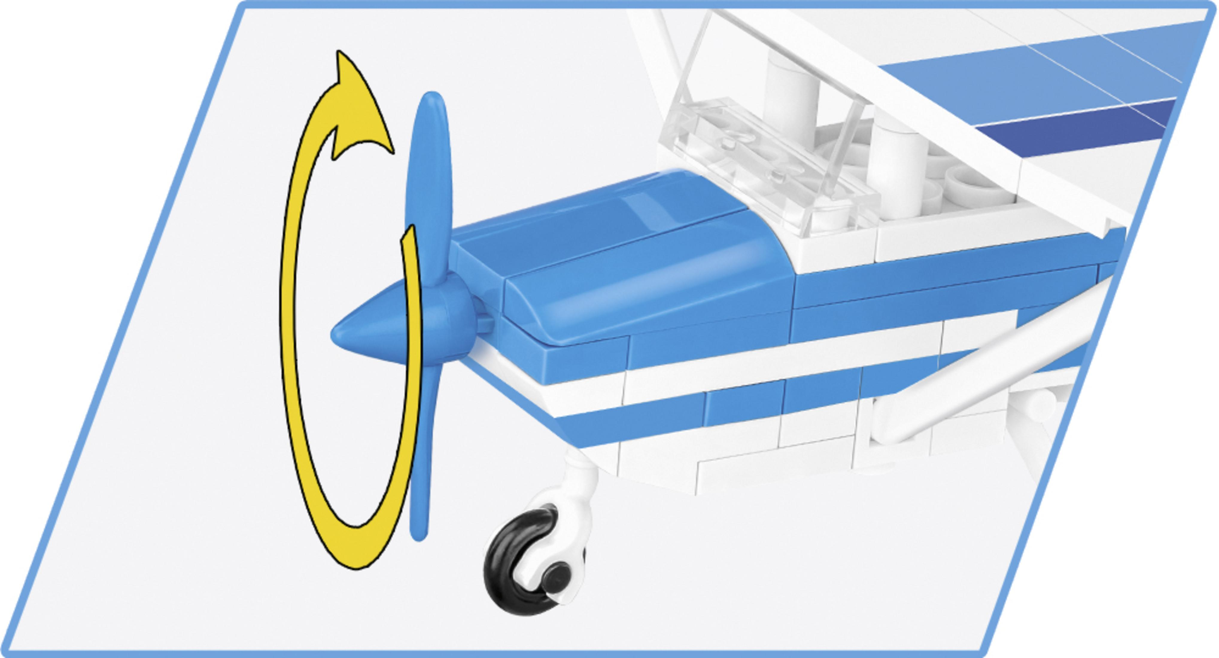 Ein kleines blau-weißes Spielzeugflugzeug. Ein gelber Pfeil zeigt die Drehrichtung des Propellers.