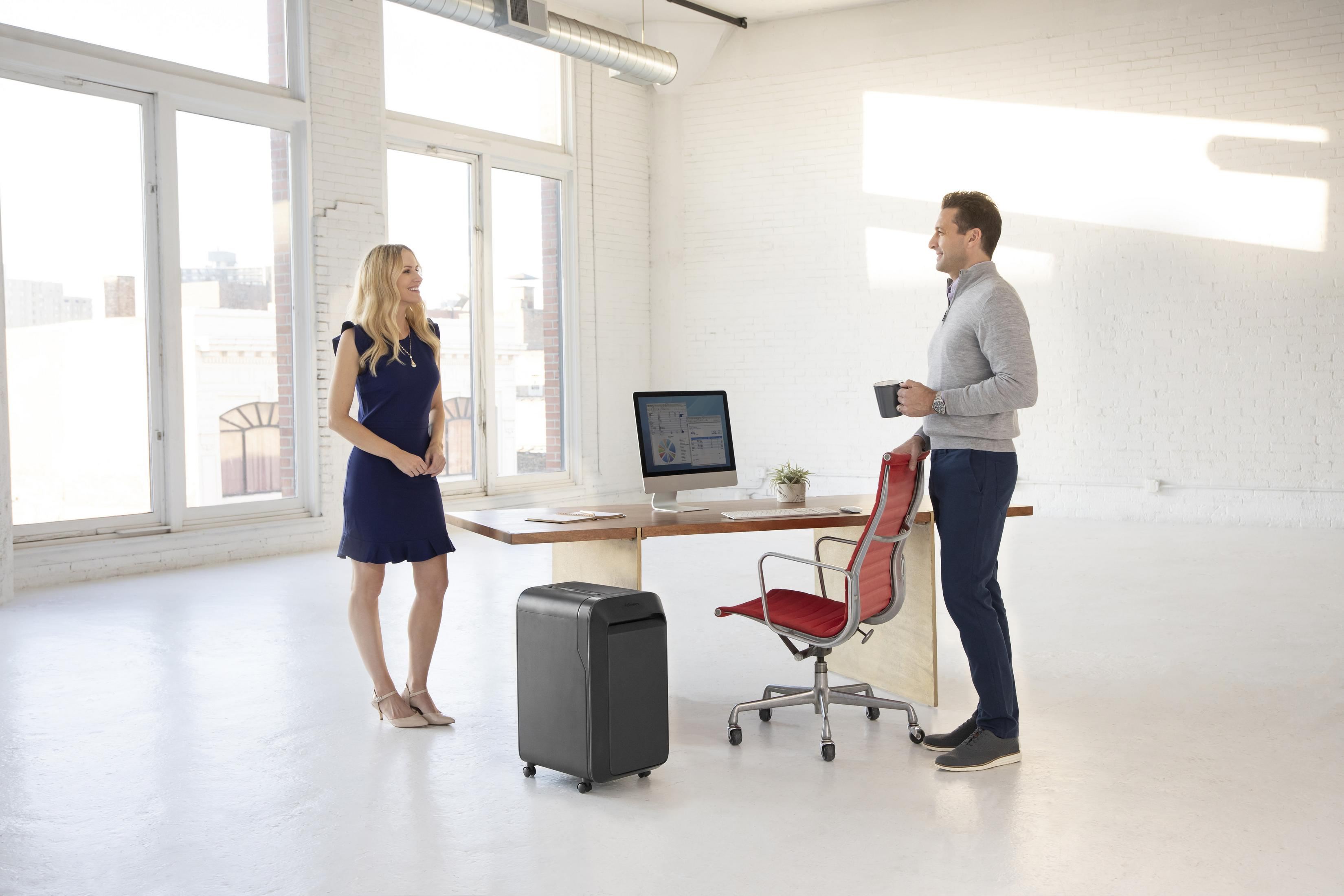 Two people in an office with a paper shredder and a computer on the desk.