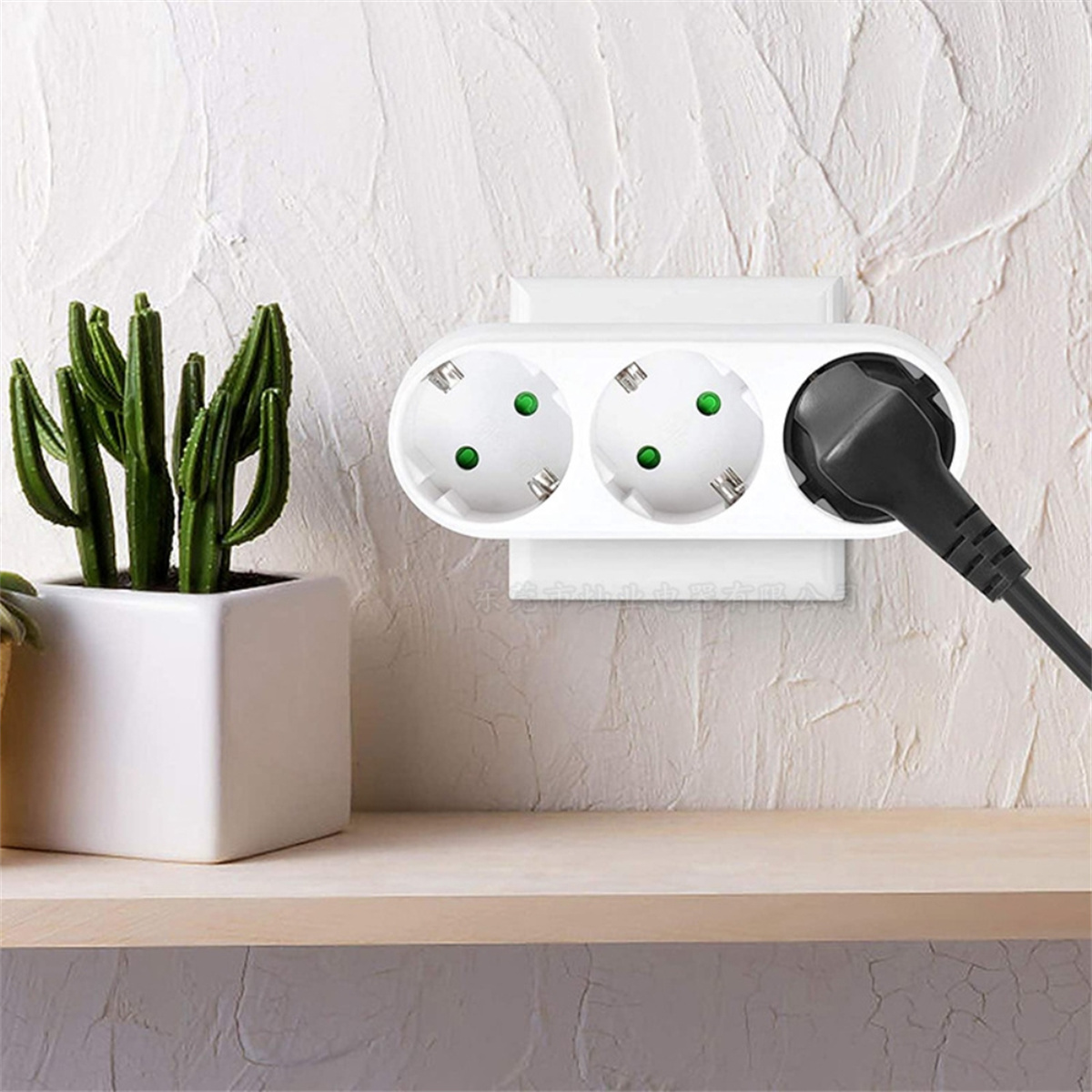 Weiße Steckdose mit drei Steckdosen und einem schwarzen Stecker an einer Wand mit Pflanze.