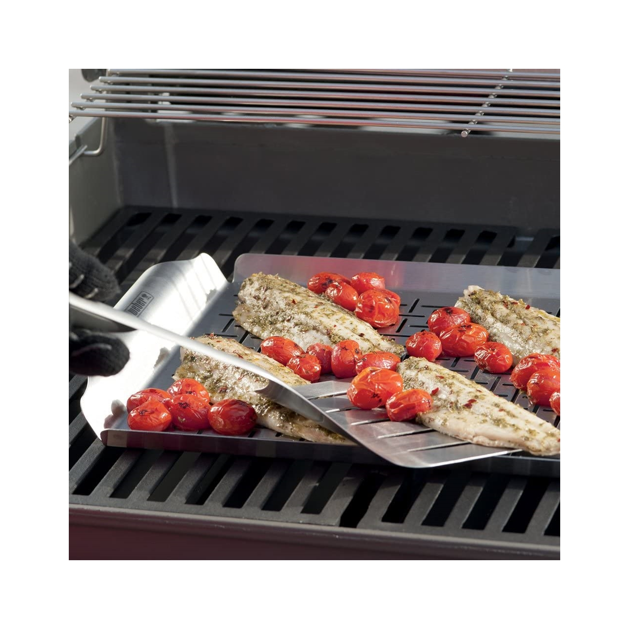 Filetes de pescado a la parrilla y tomates en una bandeja de parrilla, con pinzas.