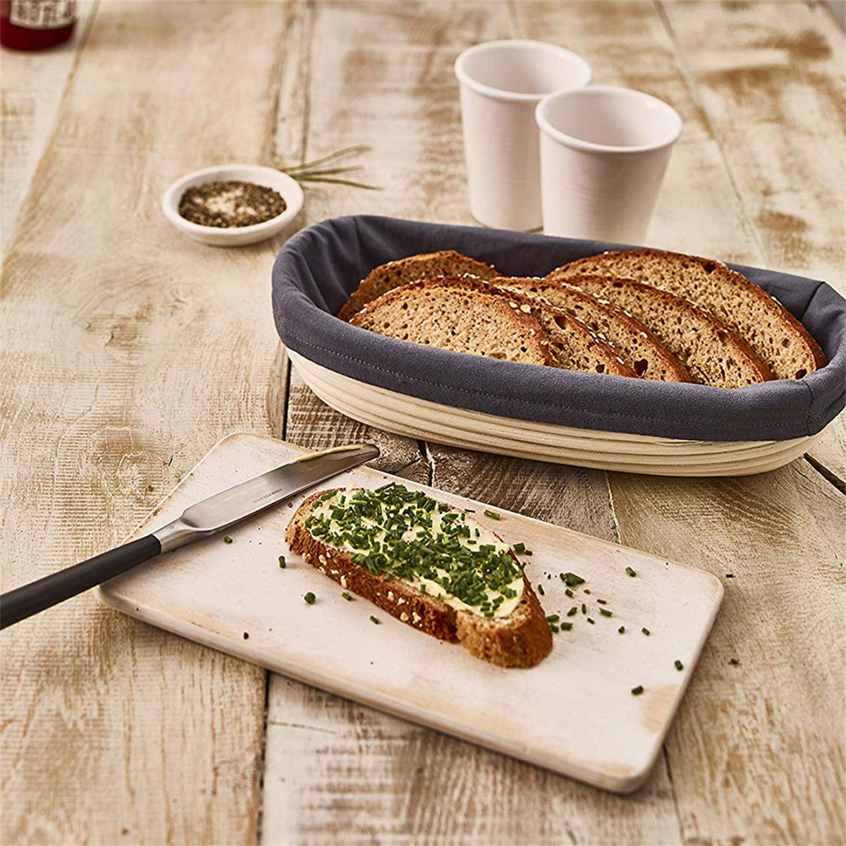 Geschnittenes Brot im Korb, Buttertoast mit Schnittlauch auf einem Brett. Salz und Pfeffer in Schalen.