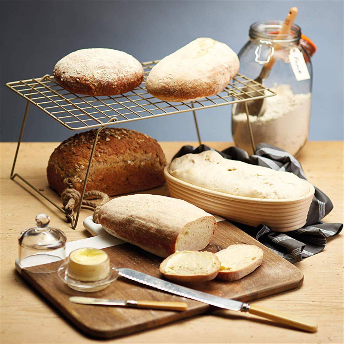 Verschiedene Brote auf einem Holztisch. Enthält einen Drahtrost, Brot, Butter und Mehl in einem Glas.
