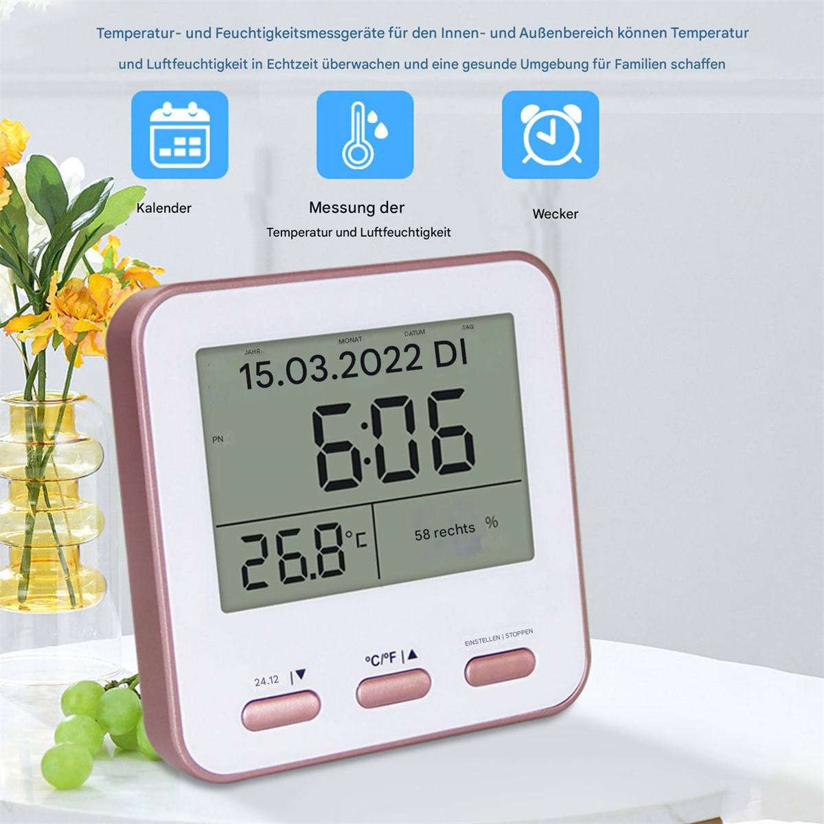 Digitaluhr zeigt Datum, Uhrzeit und Temperatur. Blumen und Trauben sind im Hintergrund.