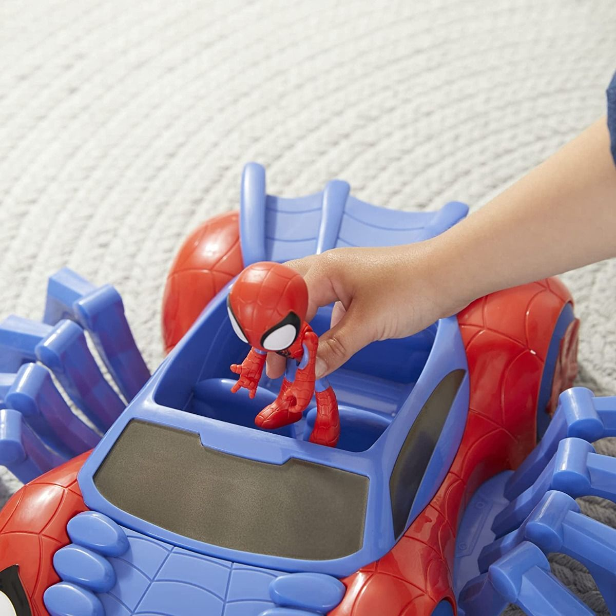 La main d'un enfant plaçant une figurine de Spider-Man dans une voiture jouet.