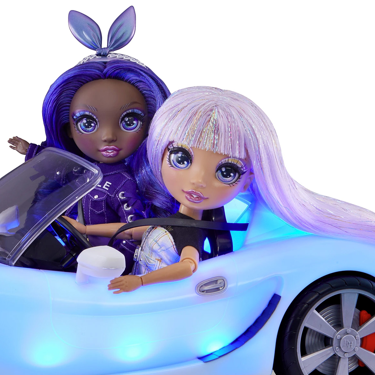 Zwei Puppen in einem blau leuchtenden Auto. Eine fährt, die andere sitzt auf dem Beifahrersitz. Weißer Hintergrund.