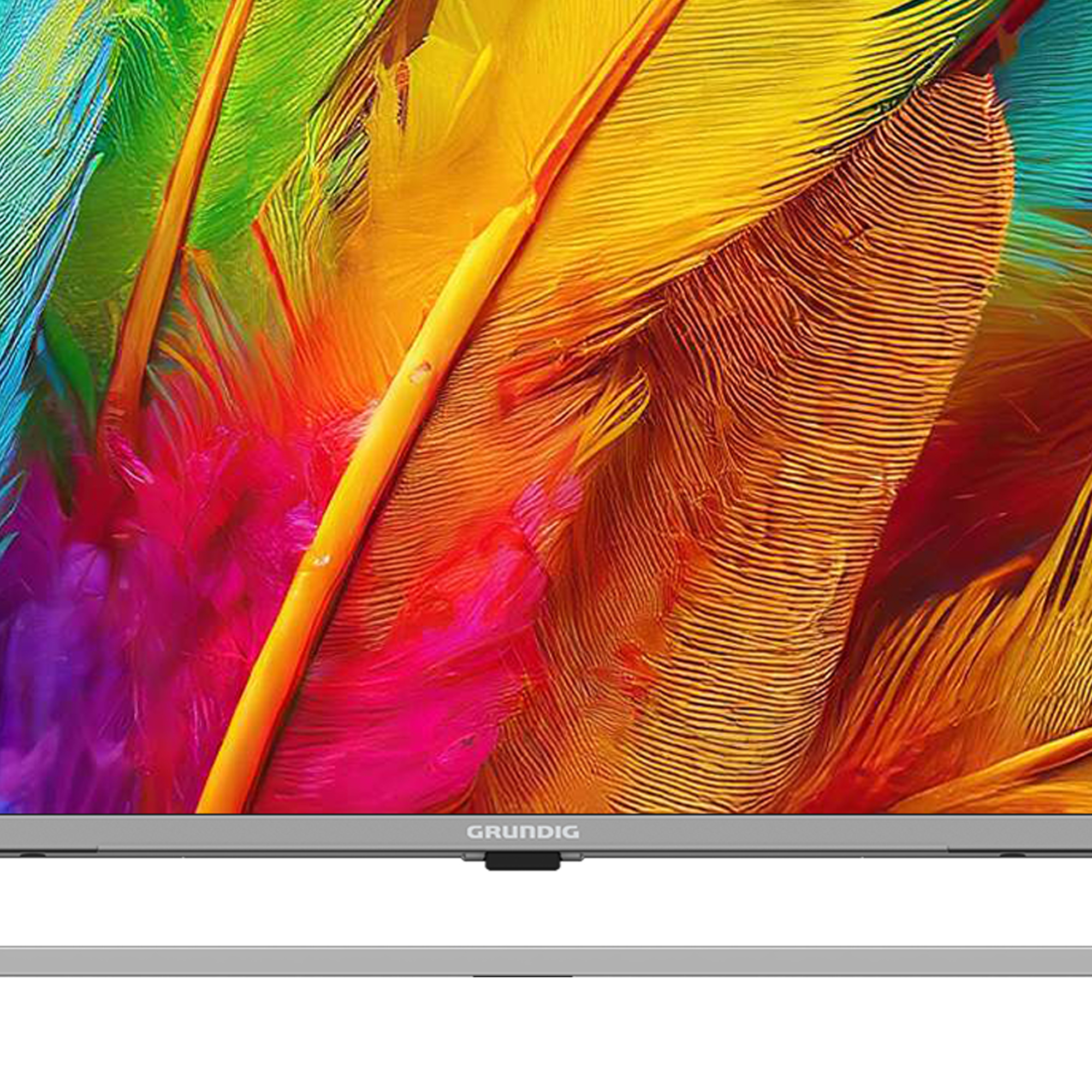 Ein Grundig-TV-Bildschirm zeigt bunte Federn in Rot, Gelb, Orange und Grün. Der Fernseher steht auf einem grauen Ständer.