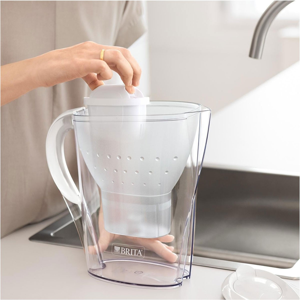 Eine Person befüllt einen Wasserfilter-Krug mit Leitungswasser, Wasserhahn sichtbar.