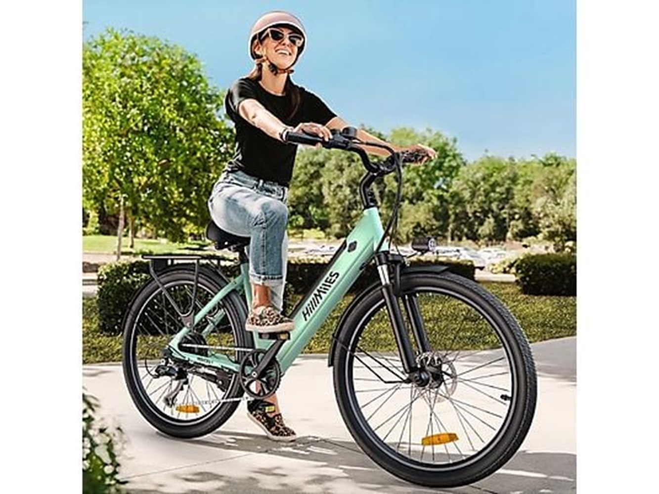 Eine Frau fährt mit einem mintgrünen E-Bike auf einer asphaltierten Straße, trägt Helm und Sonnenbrille.
