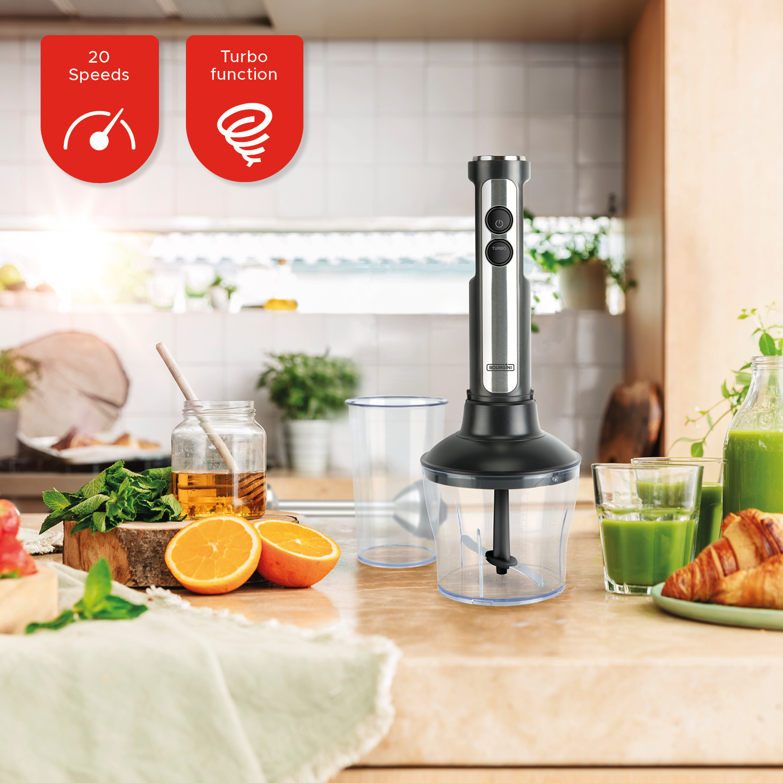 Blender ręczny z sokiem i owocami na stole. Etykiety prędkości i funkcji turbo po lewej stronie.