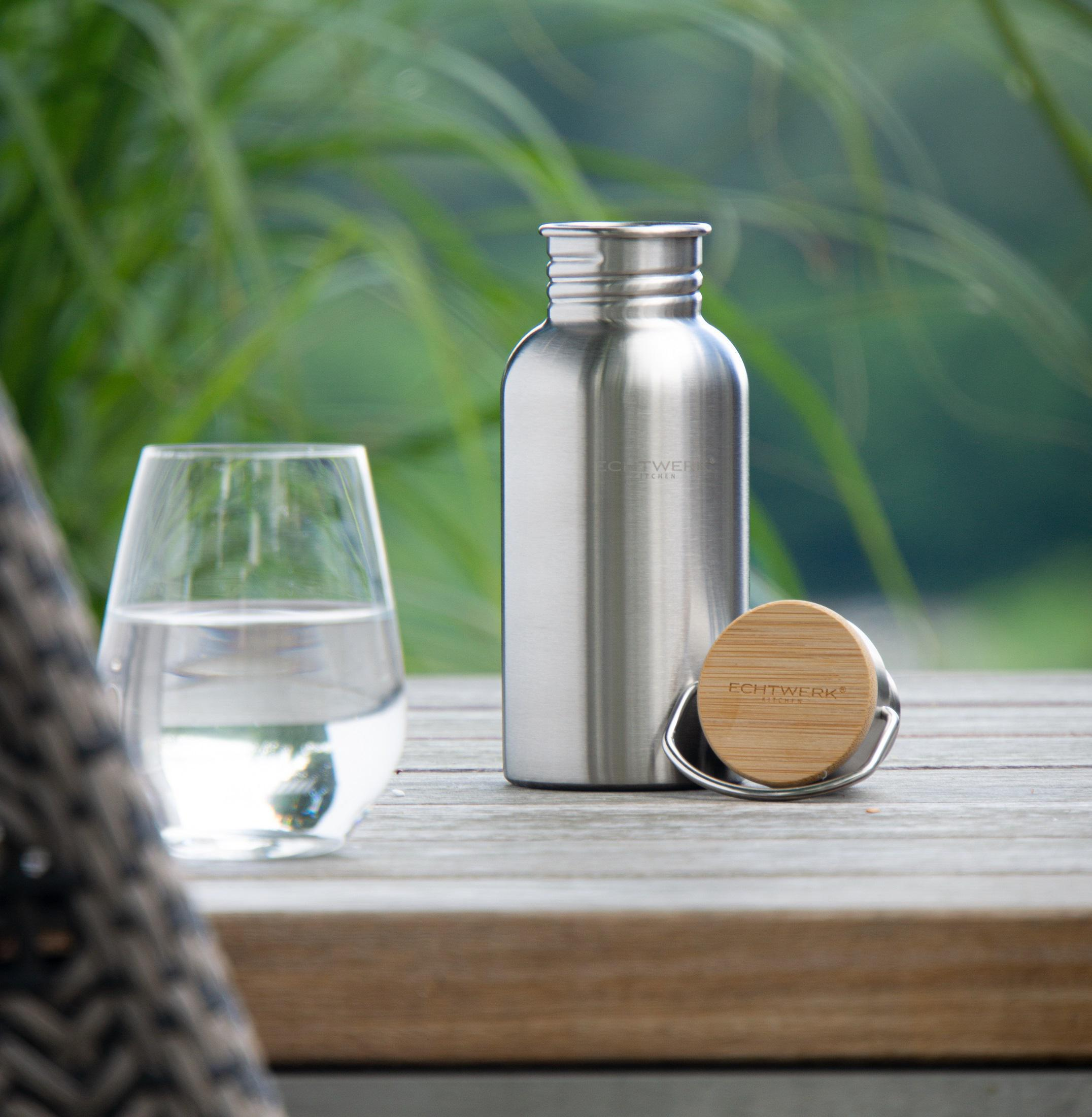 Ein Glas Wasser, eine Metall-Wasserflasche und ihr Holzdeckel auf einem Holztisch.
