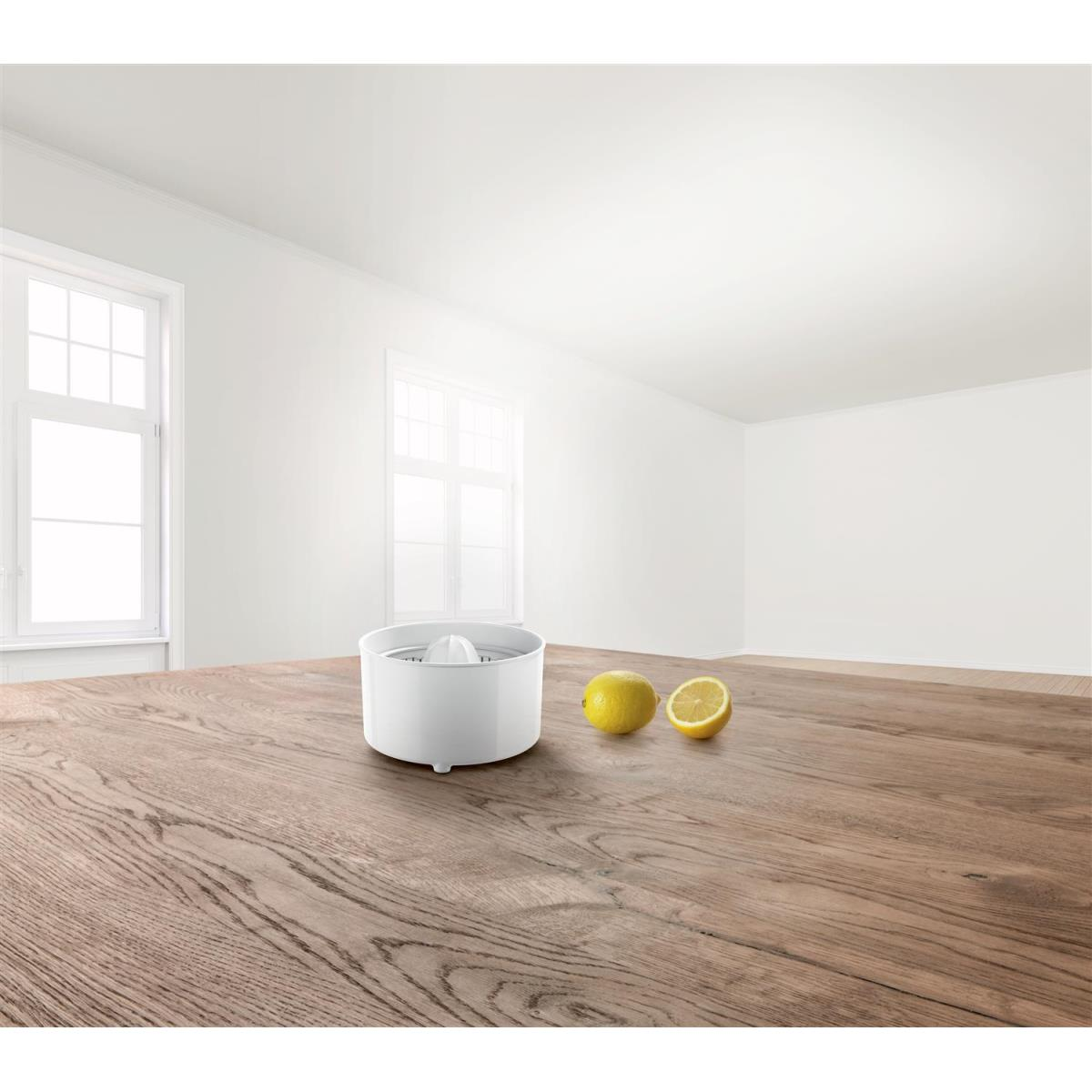 Biała wyciskarka do owoców i dwa cytryny na drewnianym stole. Biały pokój z oknami.