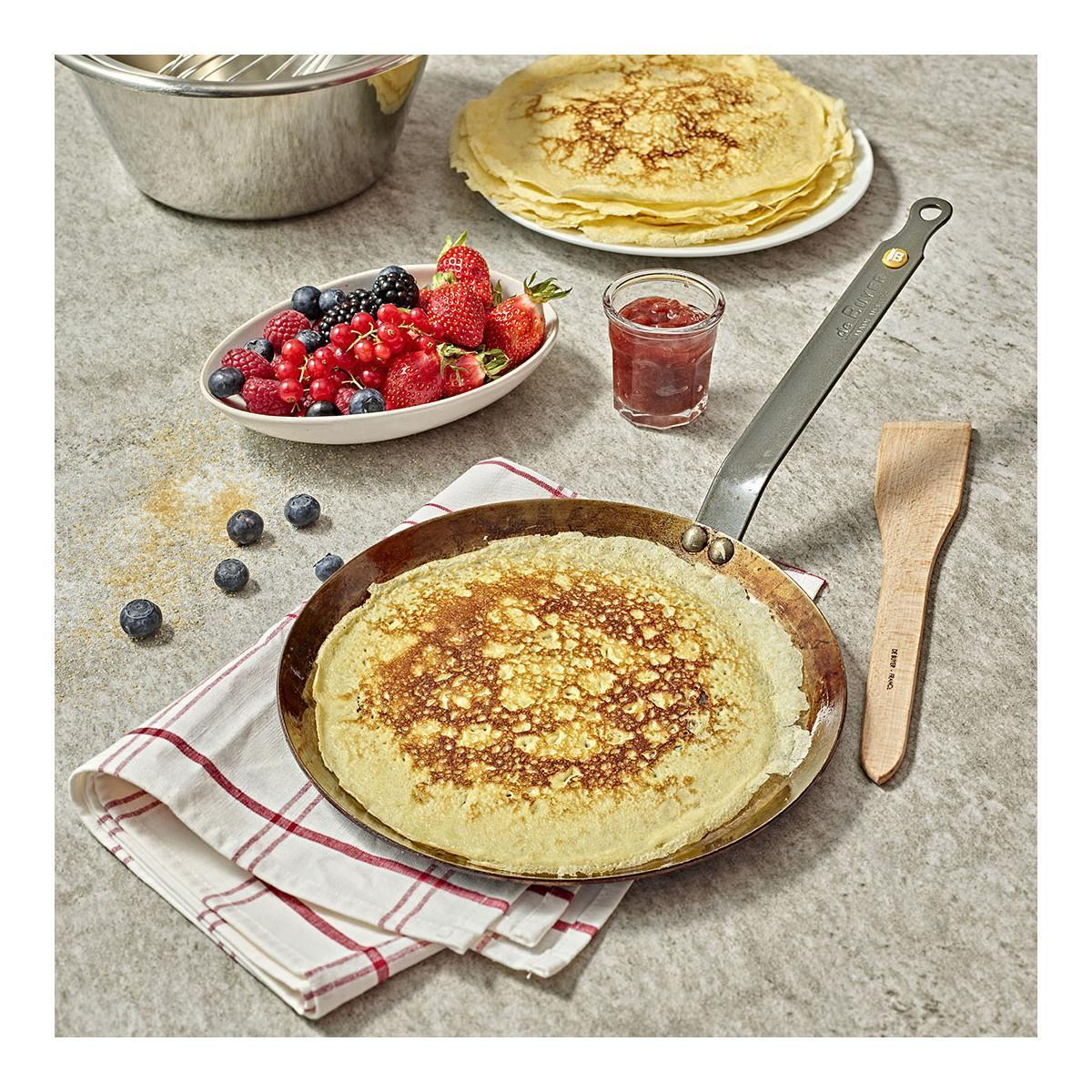 Pfannkuchen in Pfanne, Beeren, Marmelade und Holzspatel auf Stein.