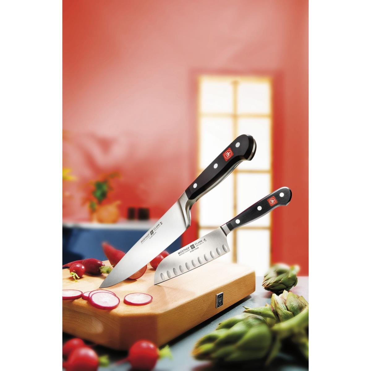 Zwei Messer mit schwarzem Griff auf einem Holzbrett mit rotem Gemüse. Roter Hintergrund.