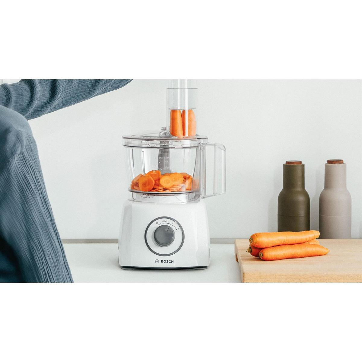 Biały robot kuchenny z krojonymi marchewkami. Marchewki i butelki na blacie.