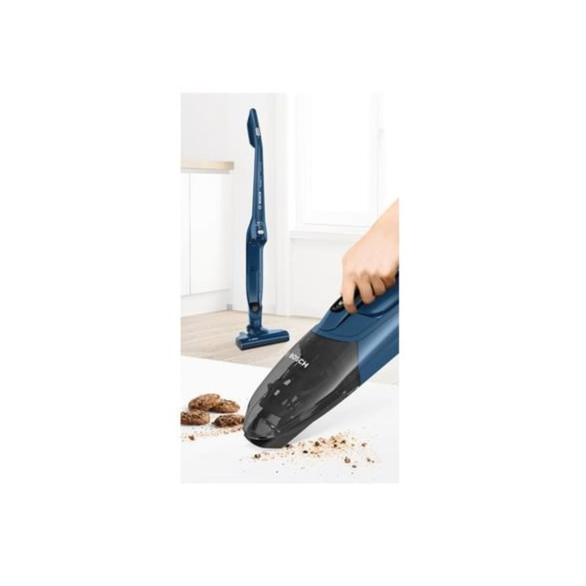 Eine Hand benutzt einen blauen Staubsauger, um Krümel auf einer weißen Oberfläche aufzusaugen. Ein zweiter Staubsauger im Hintergrund.