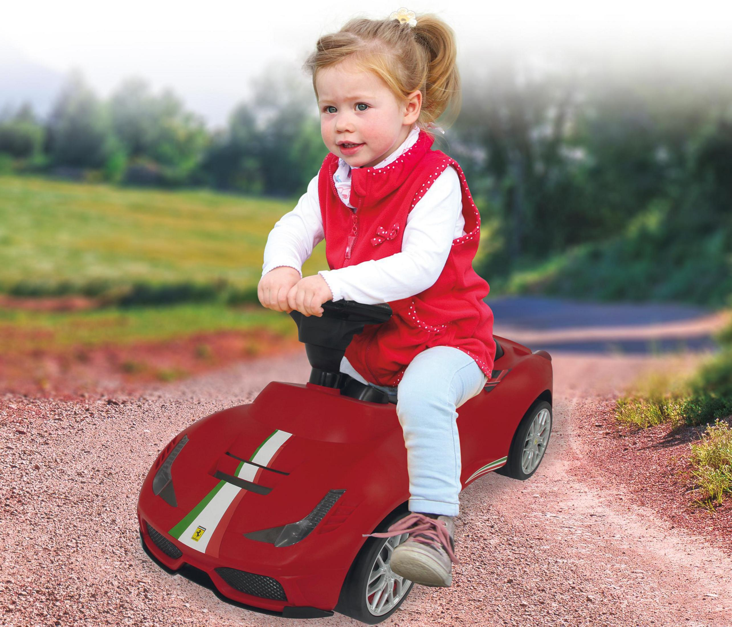 Un niño en un coche de juguete rojo en un camino de grava.