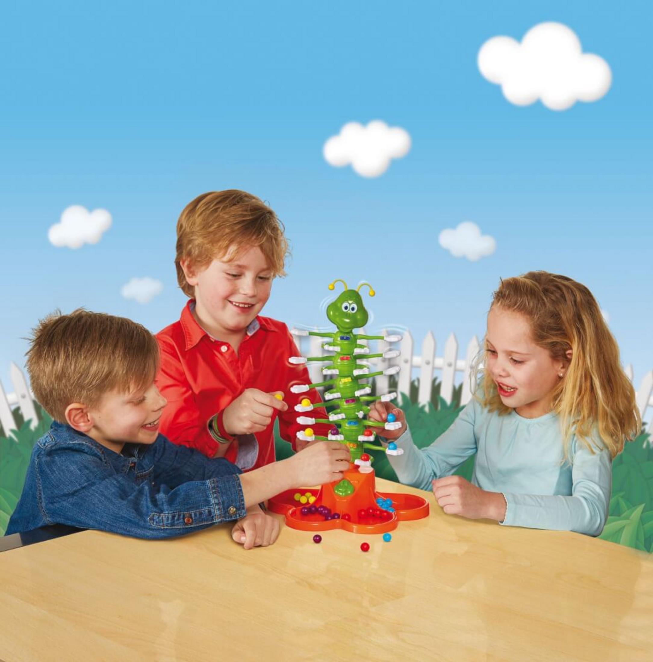 Drei Kinder spielen ein farbenfrohes Spiel. Grüne raupenartige Struktur mit bunten Kugeln.