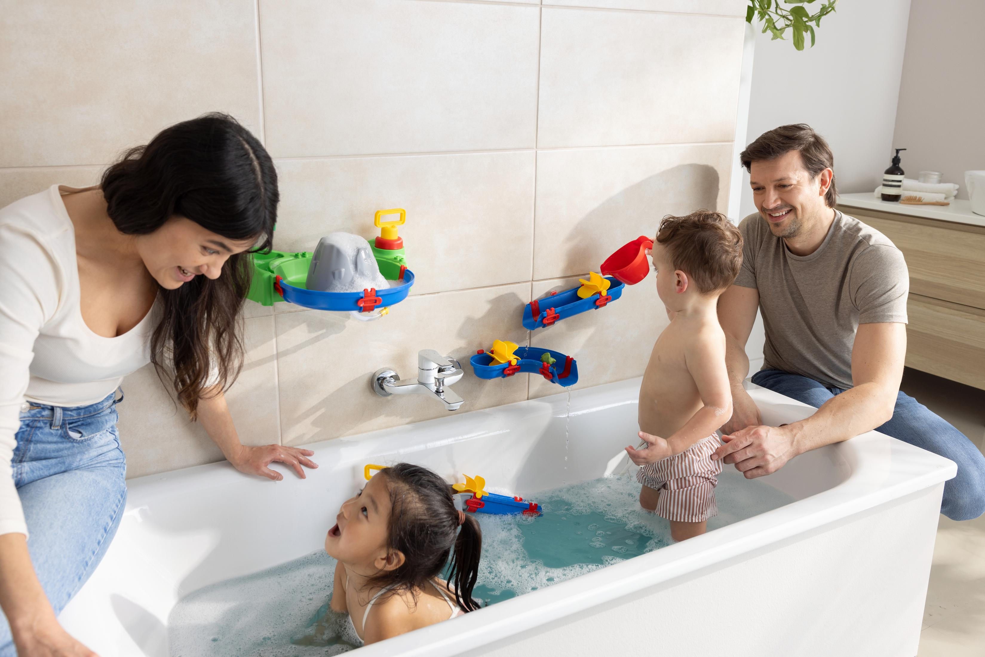 Eine Familie spielt mit einem Wasserspielzeug in einer Badewanne. Beinhaltet Eltern und Kinder.