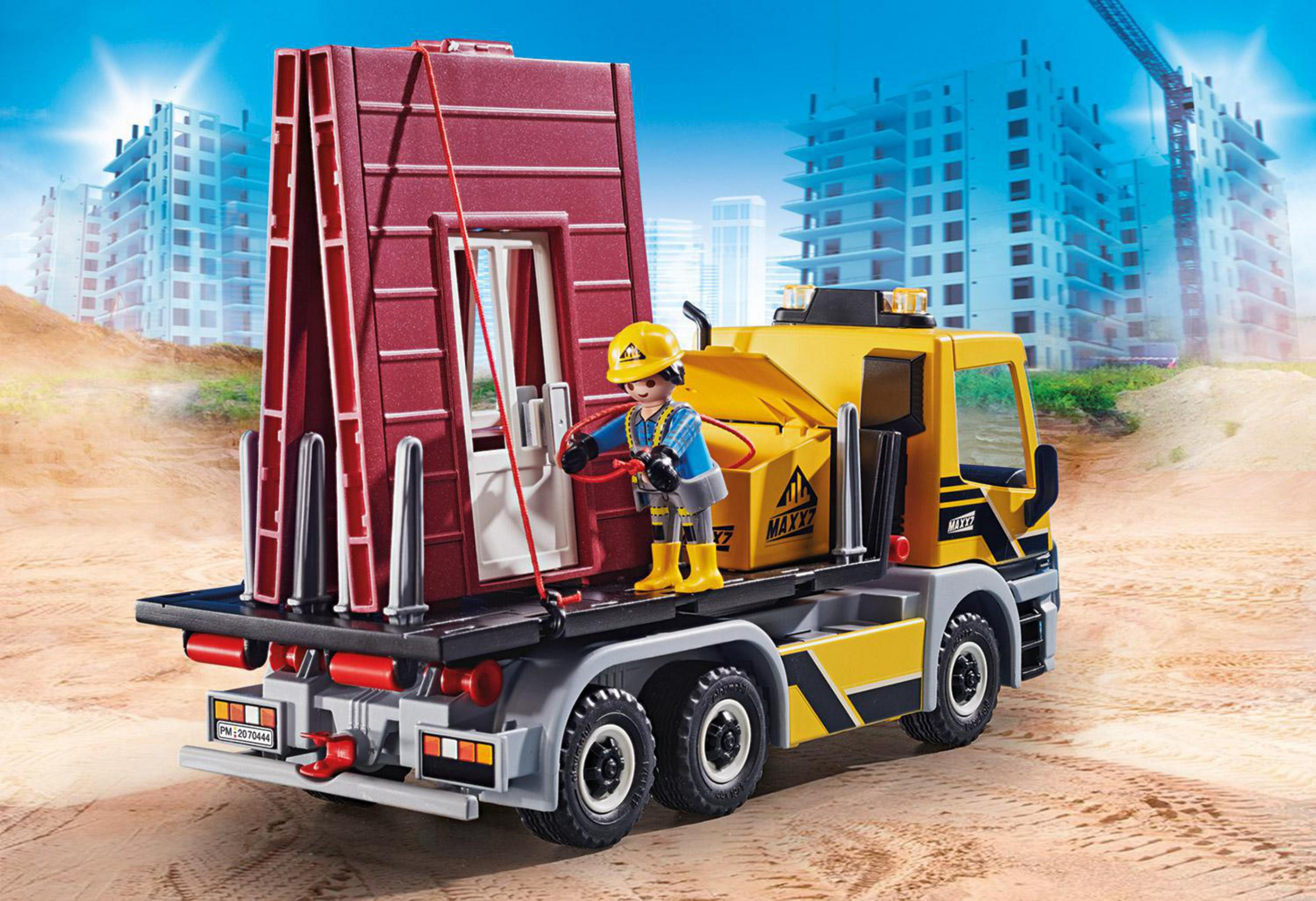 Playmobil-Baufahrzeug mit Arbeiter. Der LKW transportiert einen roten Gebäudeteil. Baustell-Hintergrund.