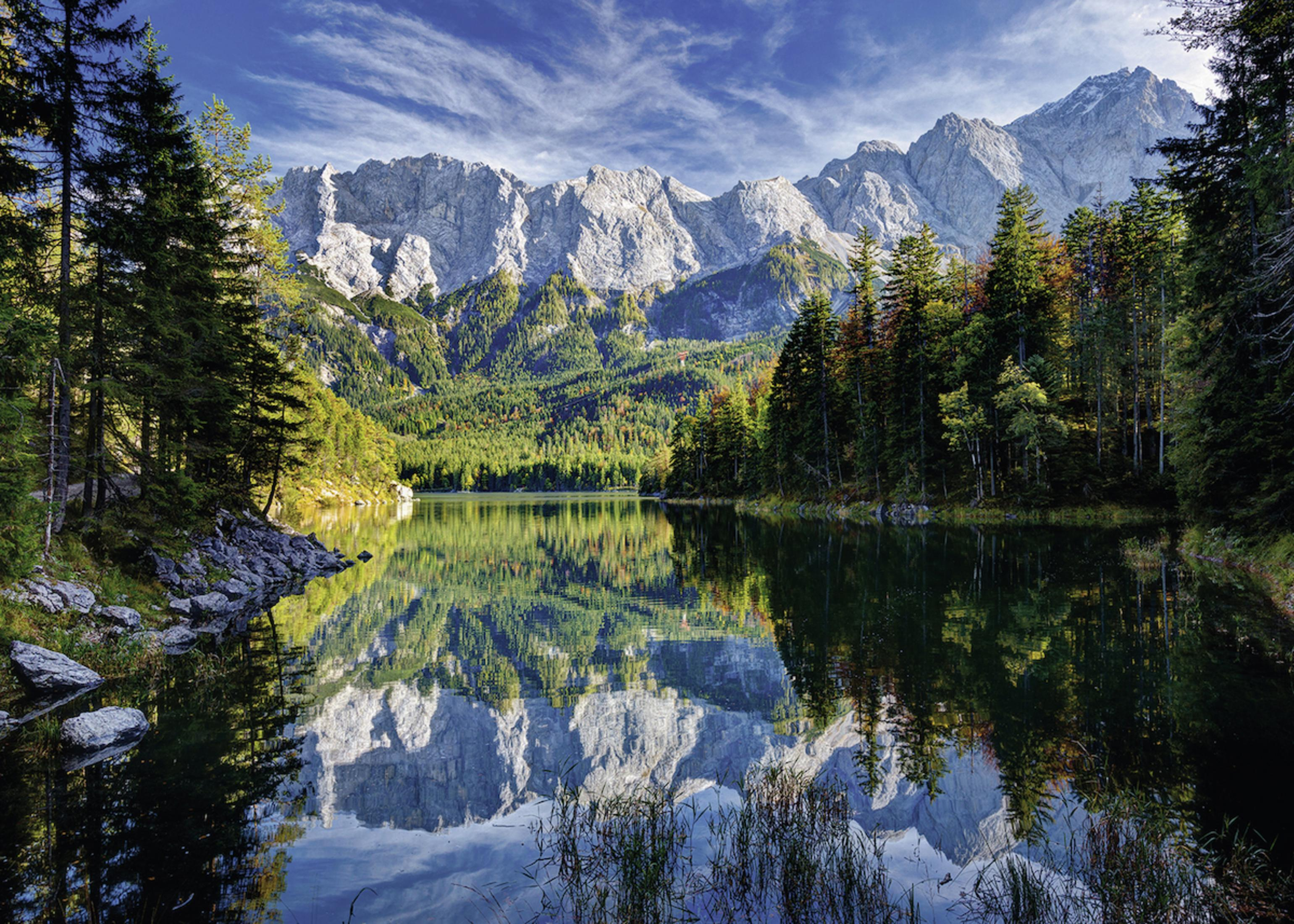 Ein klarer See, der Berge und Bäume widerspiegelt. Der Himmel hat Wolken.
