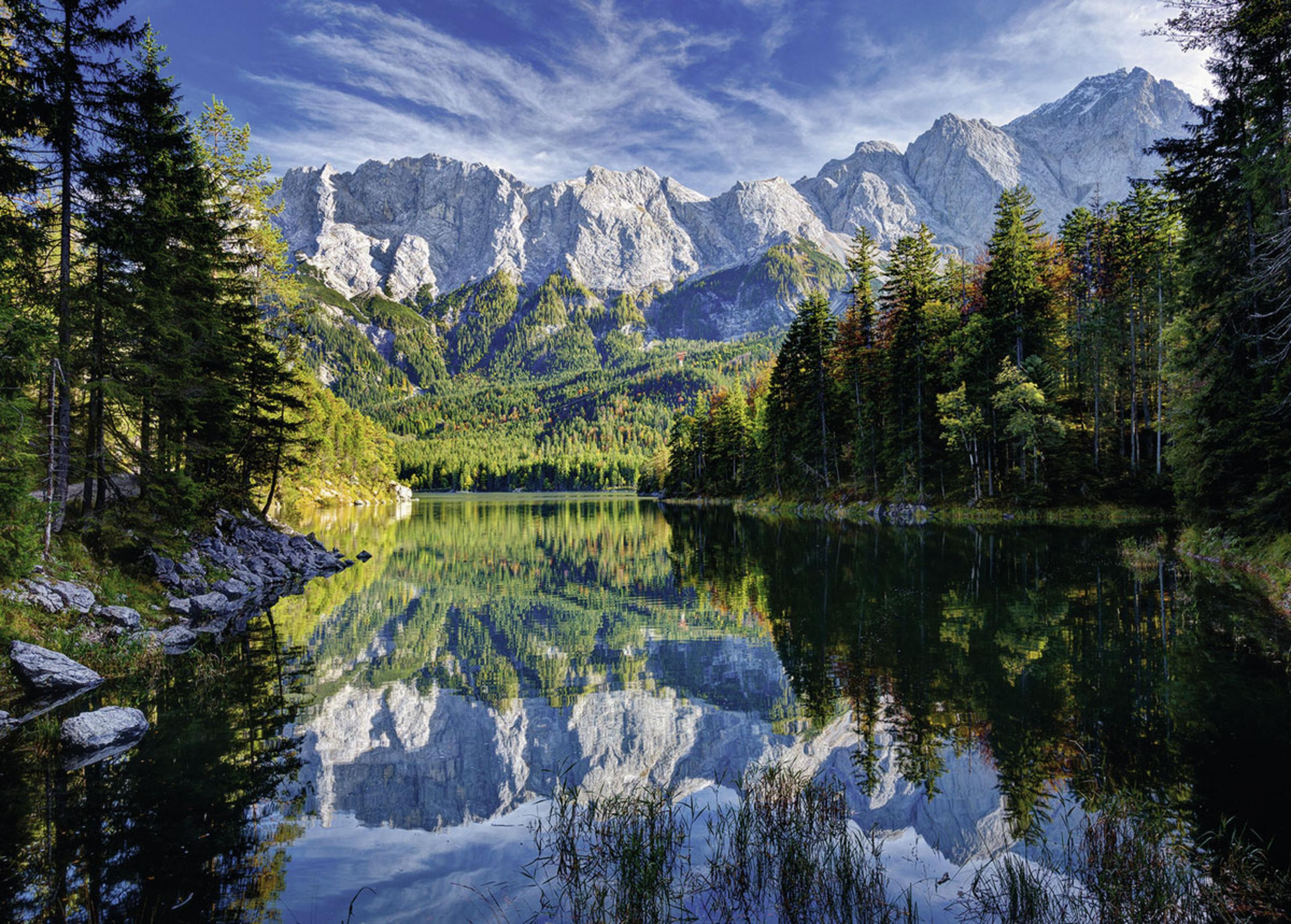 Eine Landschaft mit einem See, der Berge und Bäume unter blauem Himmel spiegelt.