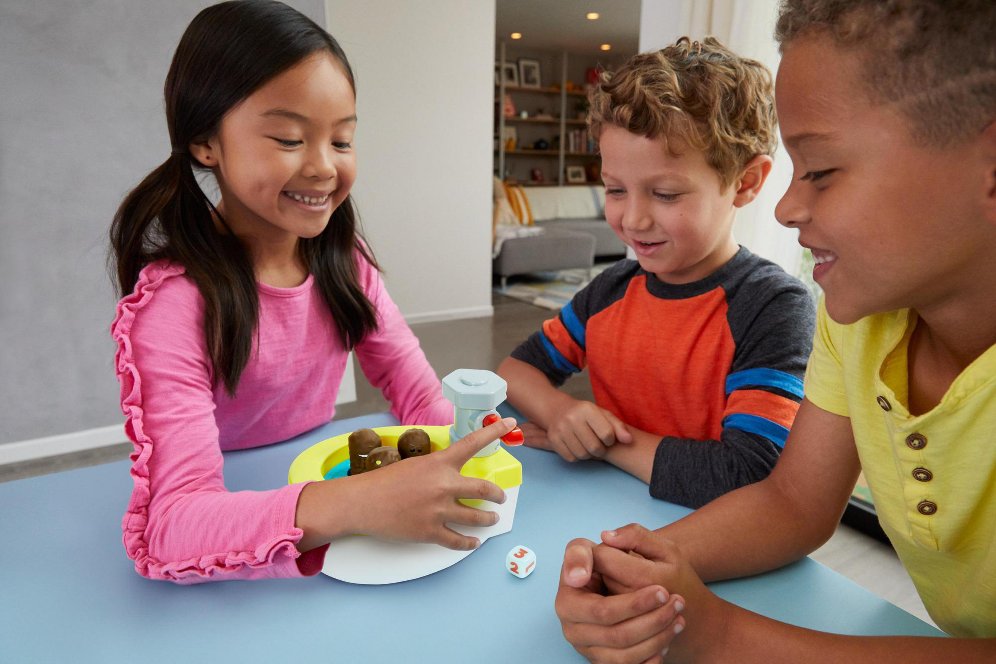 Drei Kinder spielen ein Brettspiel, farbenfrohes Spielbrett, Würfel und Spielsteine.