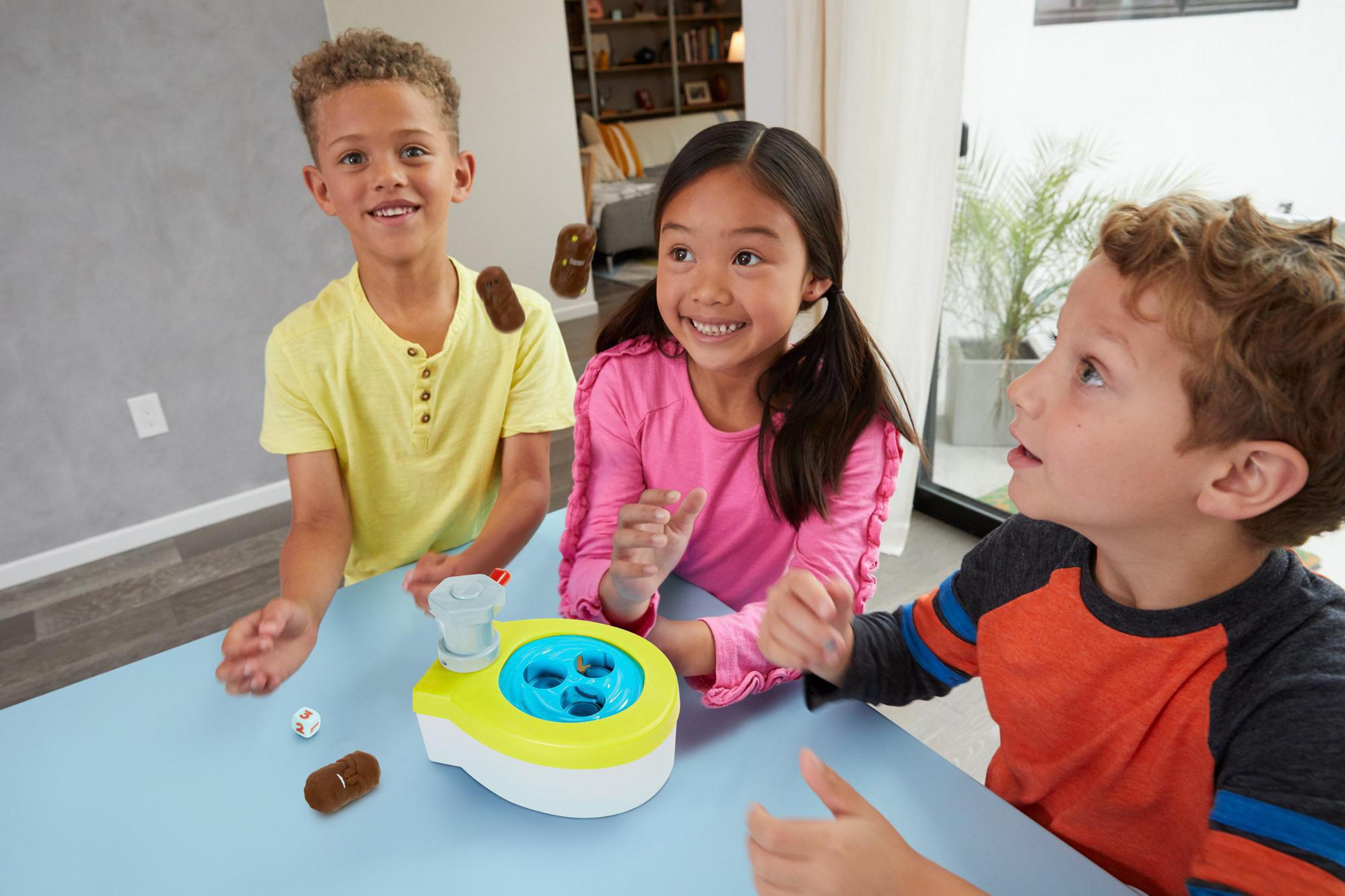 Drei Kinder spielen ein Brettspiel. Braune Formen fliegen in der Luft. Blauer Tisch. Fröhliche Gesichter.